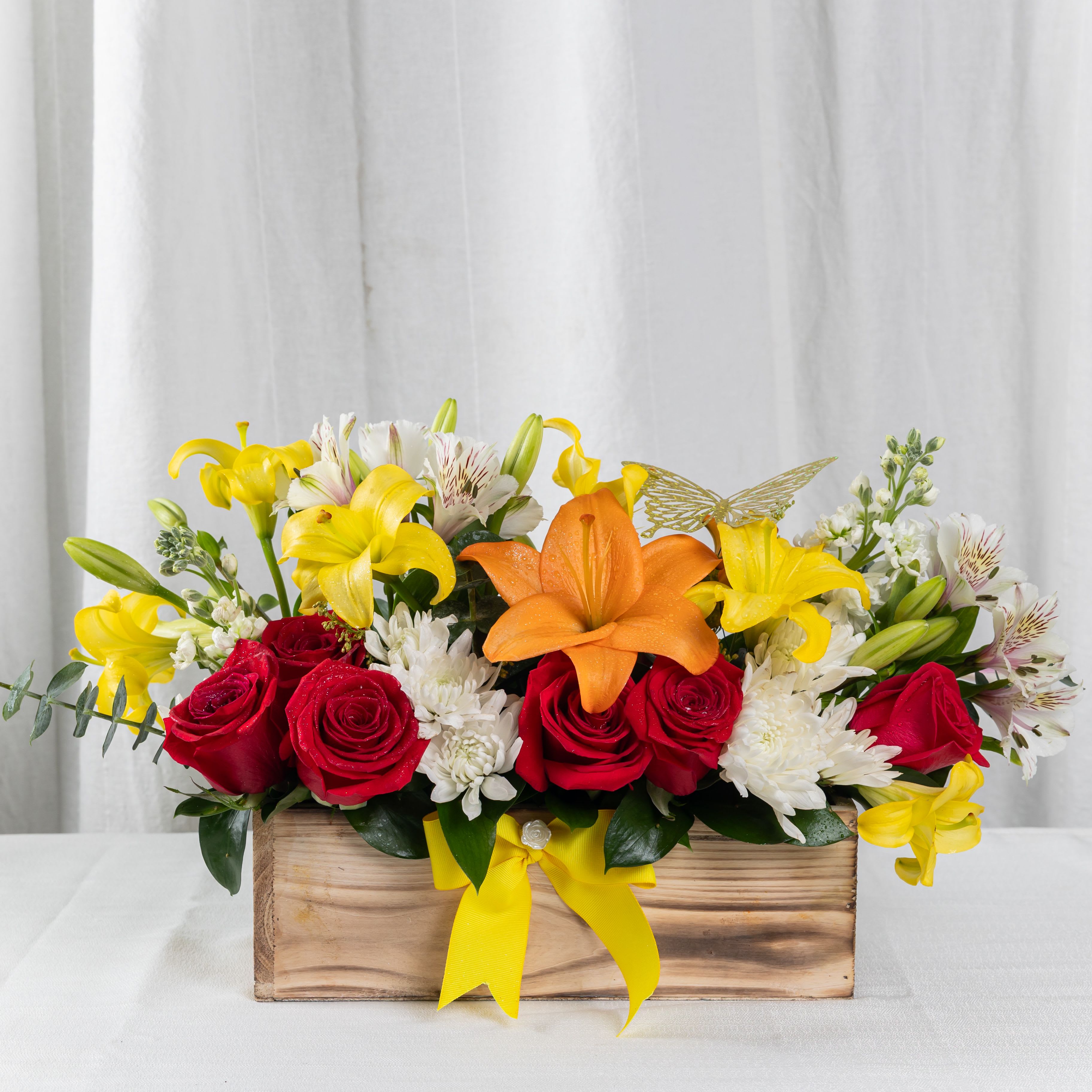 Mixed bouquet of red roses, yellow lilies, and white flowers in a wooden box