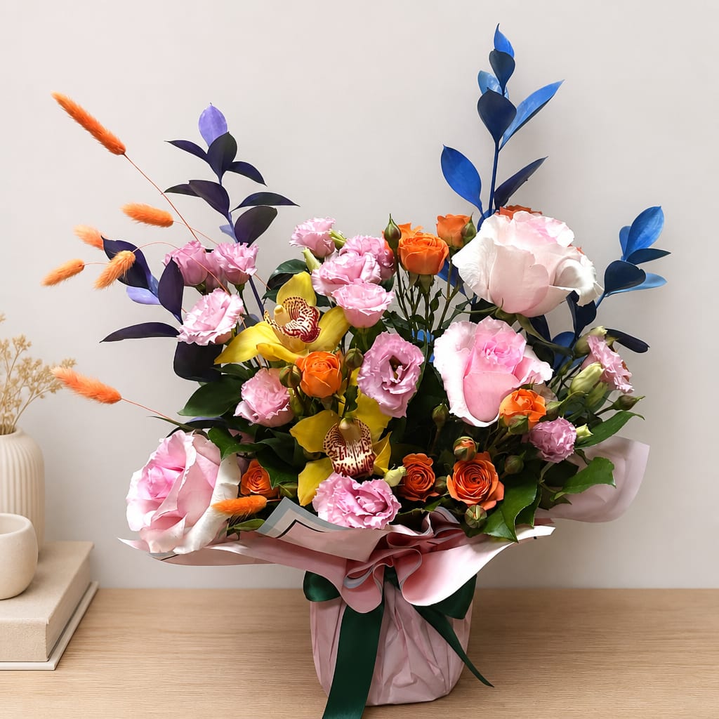 Mixed bouquet of pink, orange, yellow, and blue flowers in a wrapped container