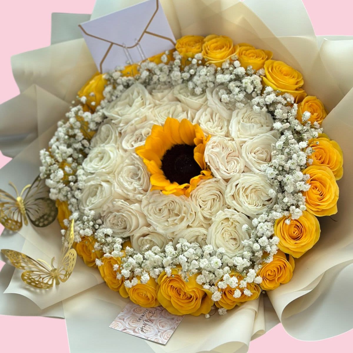 Para Ti, Con Amor - A radiant round bouquet crafted with white and yellow roses, beautifully framed by soft baby’s breath. At the center, a vibrant sunflower steals the spotlight, symbolizing light, joy, and positive energy. Available in two sizes: 25 roses and 50 roses