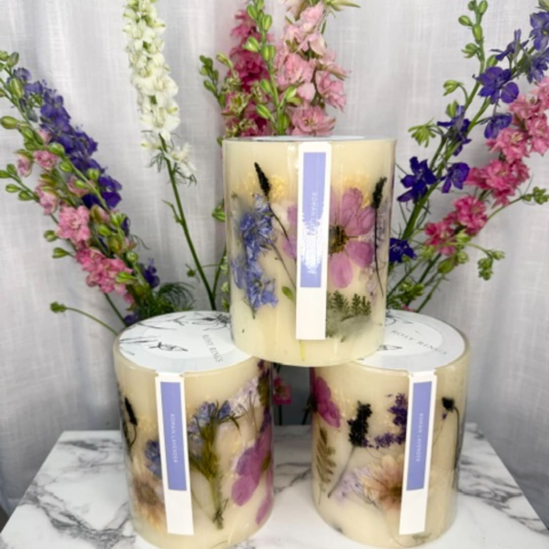 Three floral candles with pressed flowers and tall flower stems behind them
