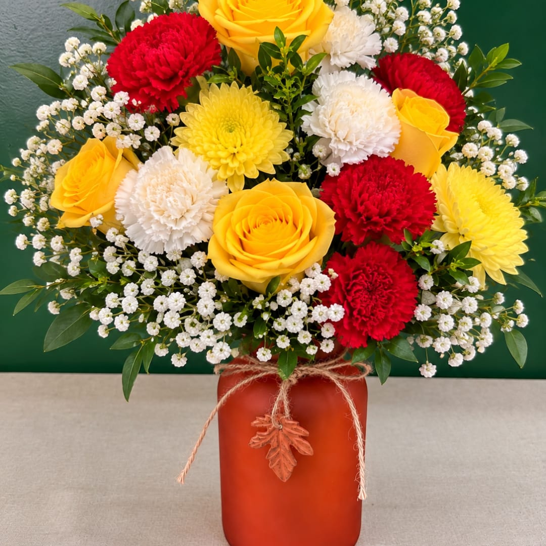 Yellow roses, red and white carnations, and baby's breath in a red vase