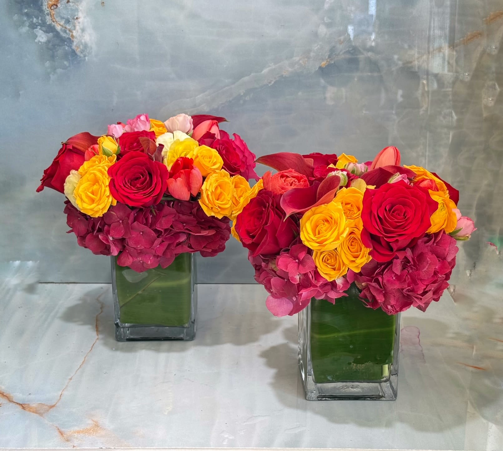 Two colorful rose arrangements in square glass vases