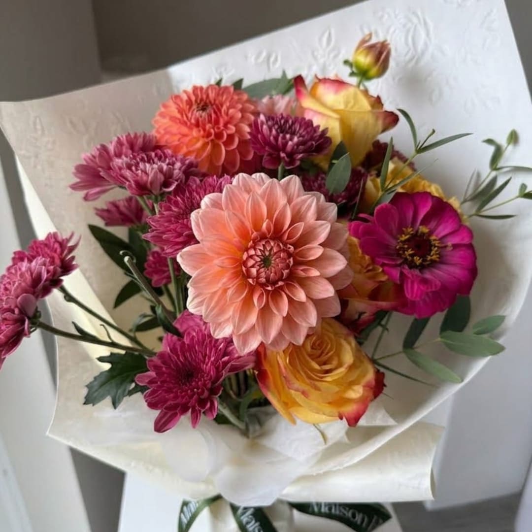 Mixed bouquet of pink, peach, and yellow flowers wrapped in white paper
