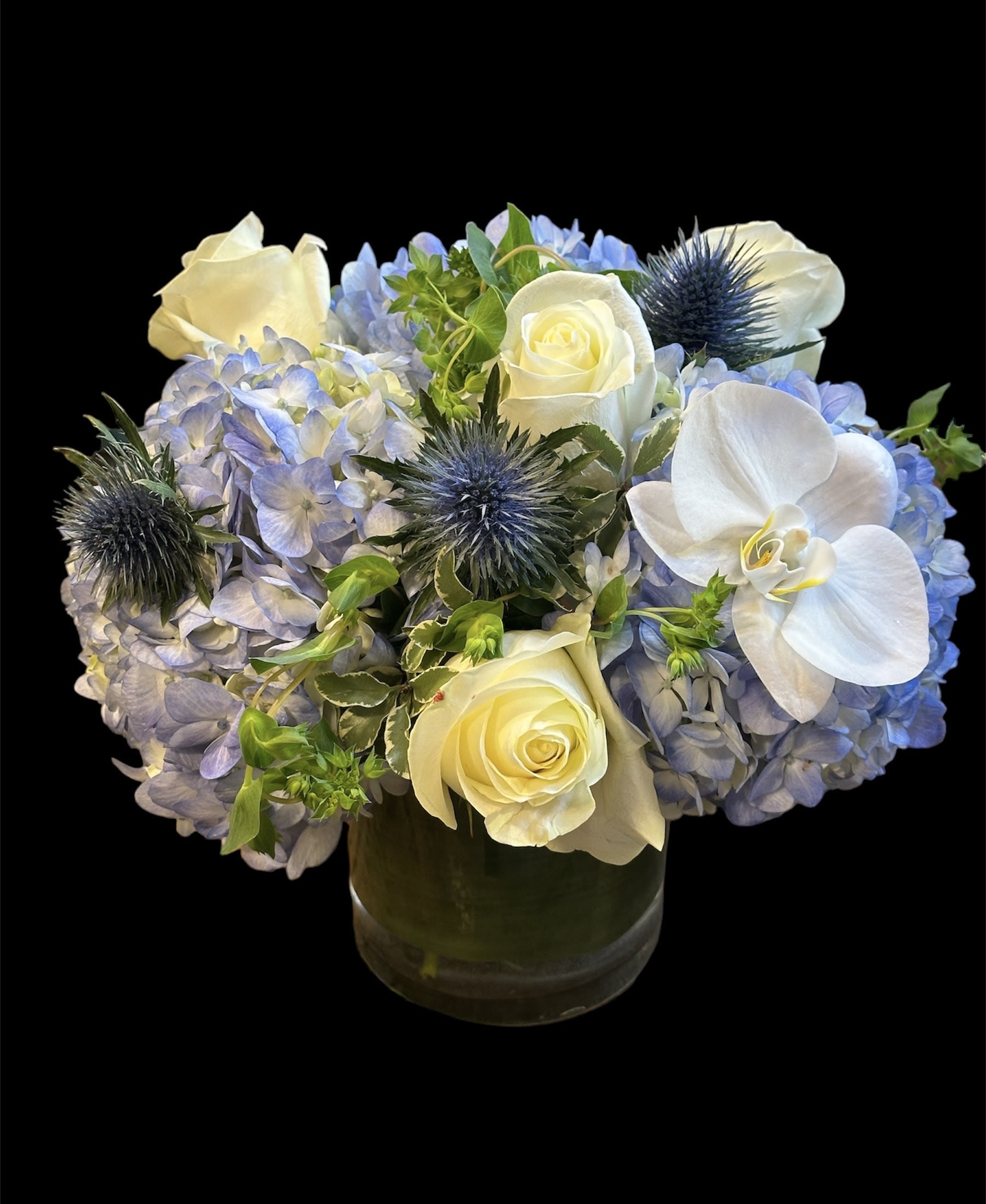 Blue hydrangeas with white roses and orchids in a glass vase