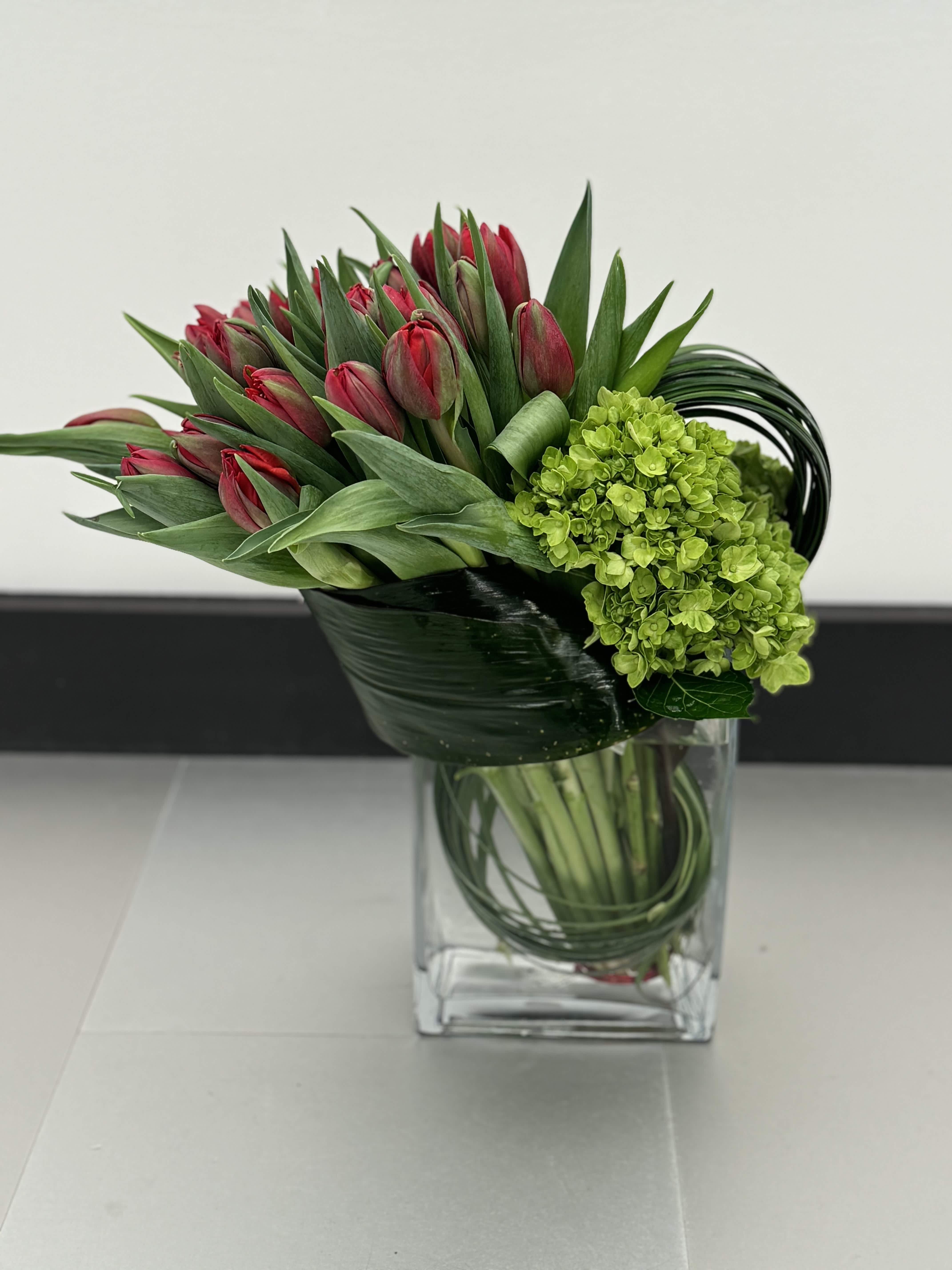 Red tulips and green hydrangea in a clear glass vase