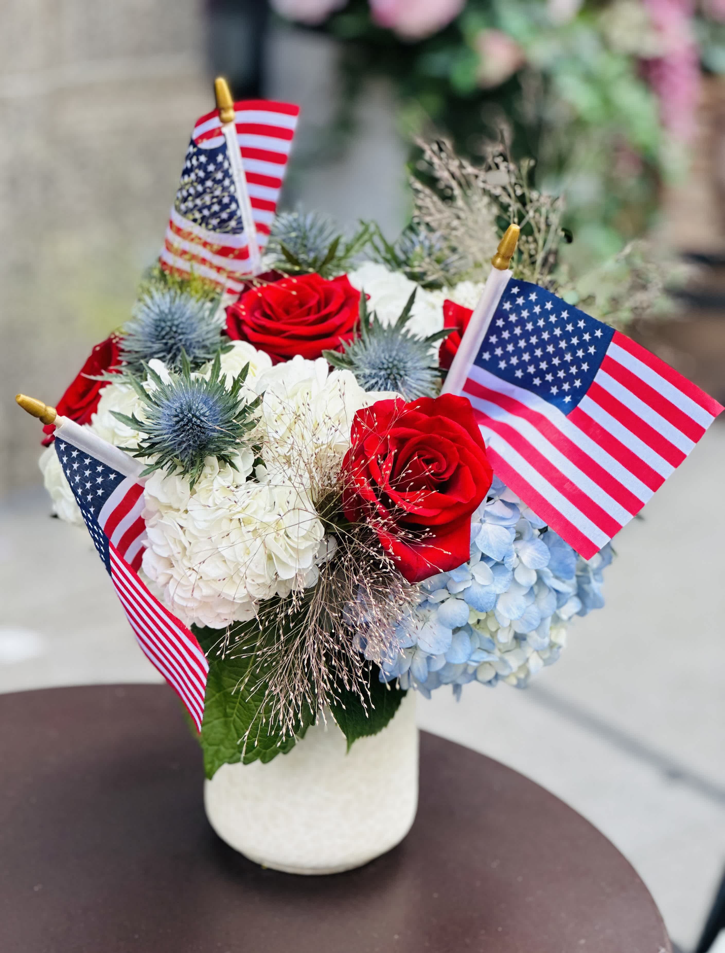 Red roses and hydrangeas in a white vase with small American flags
