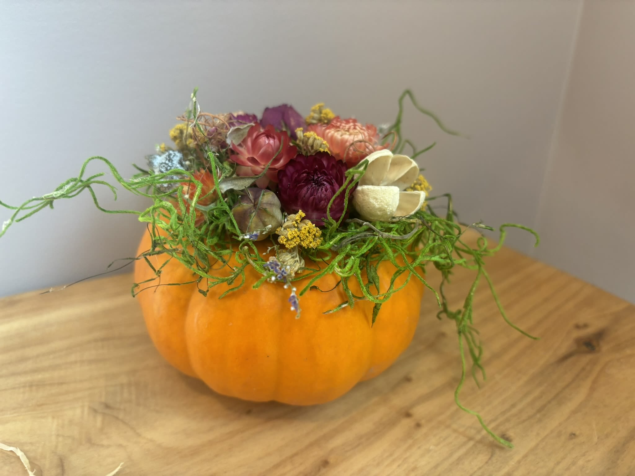 Floral arrangement in a pumpkin-shaped container with colorful blooms and curly greenery