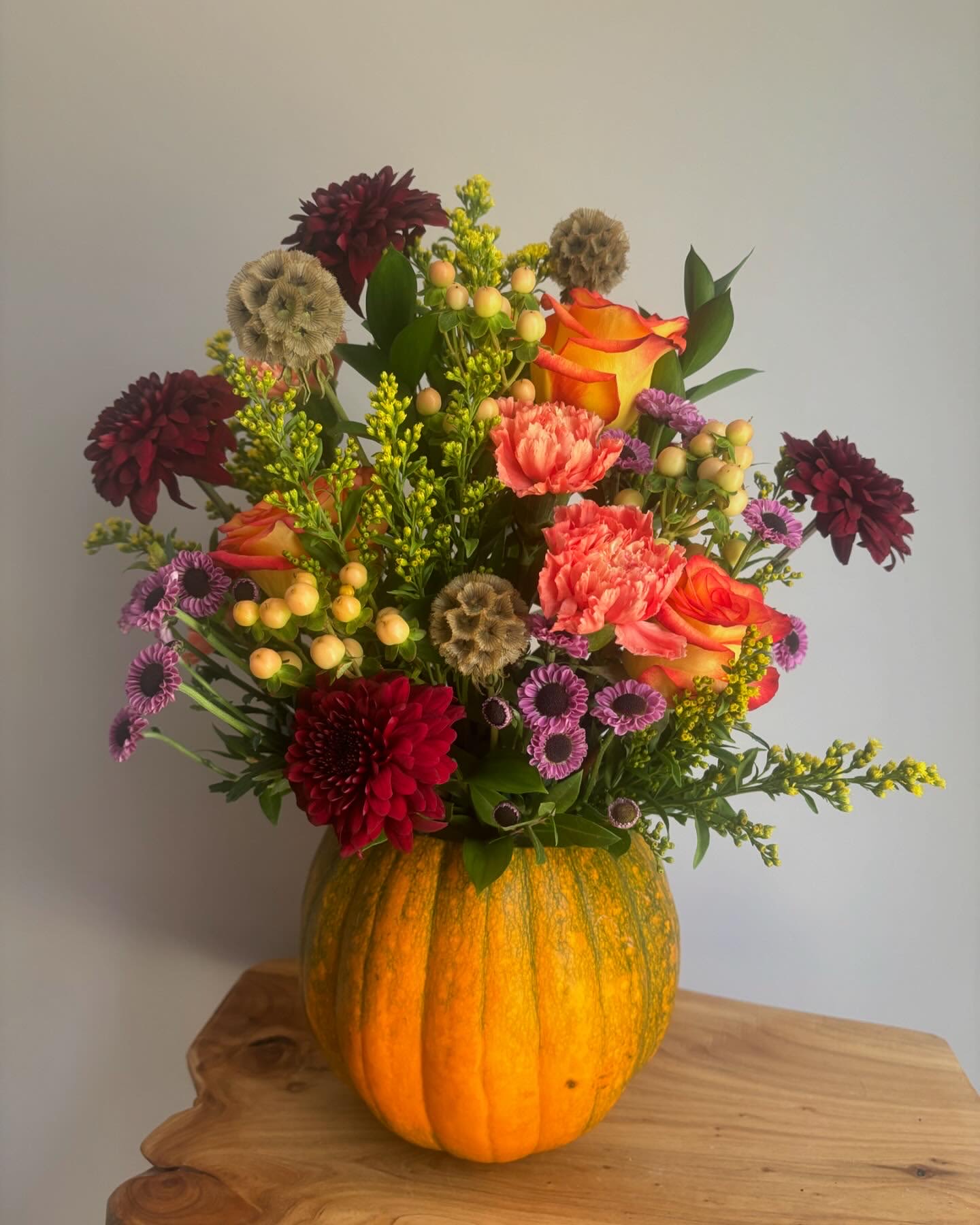 Mixed bouquet in a carved pumpkin vase with orange roses and burgundy blooms