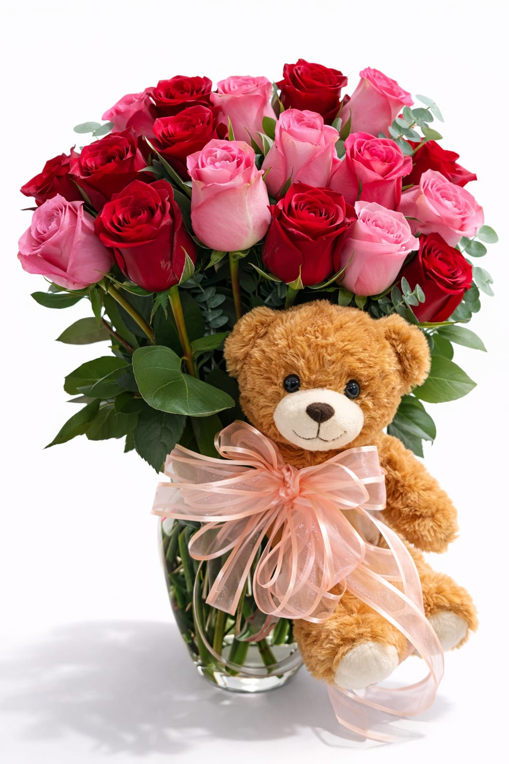 Pink and red roses in a glass vase with a teddy bear and ribbon