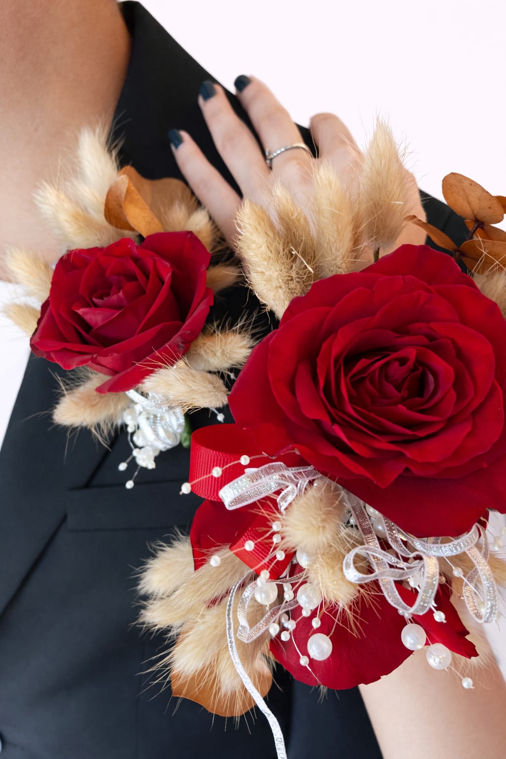 Red rose corsage with beige dried accents and ribbon on a wrist