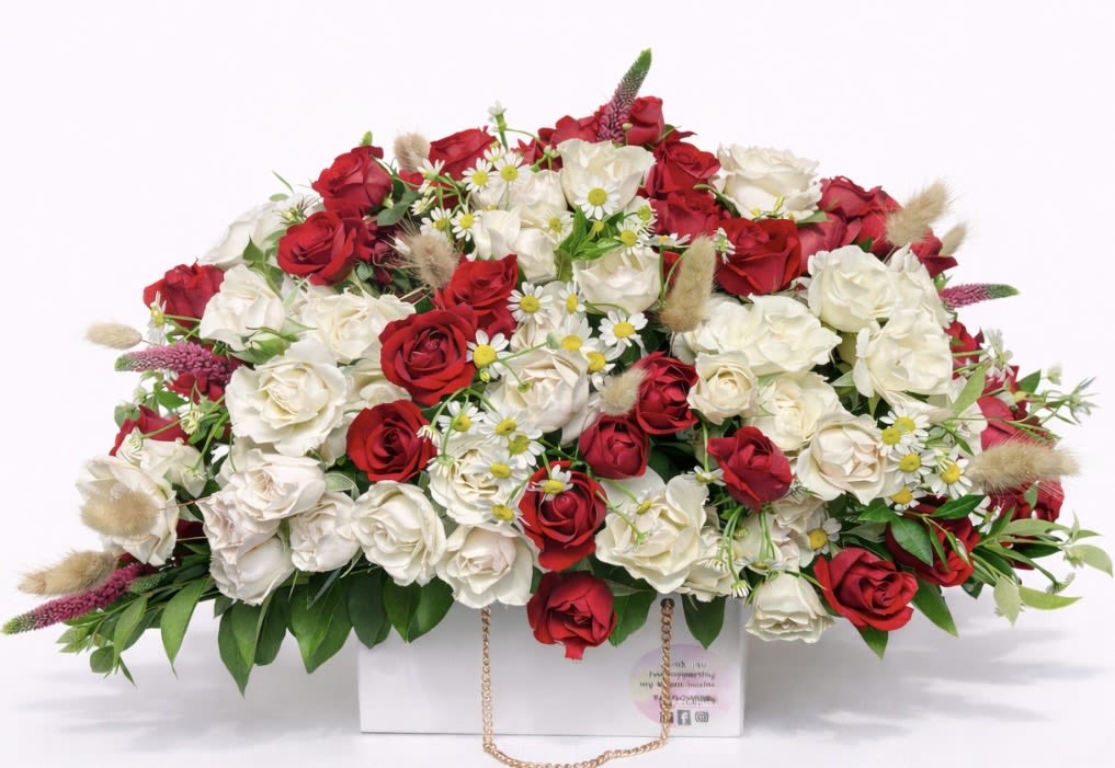 Red and white rose arrangement in a white box with small daisy accents