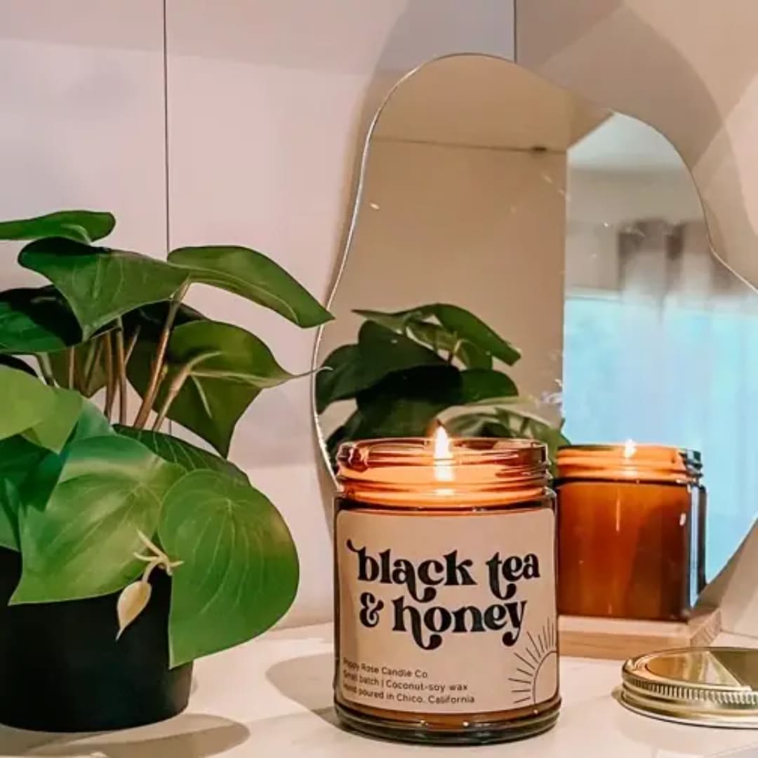 Lit amber candle jar beside a potted plant and mirror