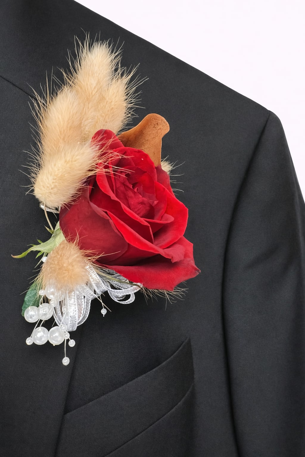 Red rose boutonniere with beige dried accents on a black suit lapel