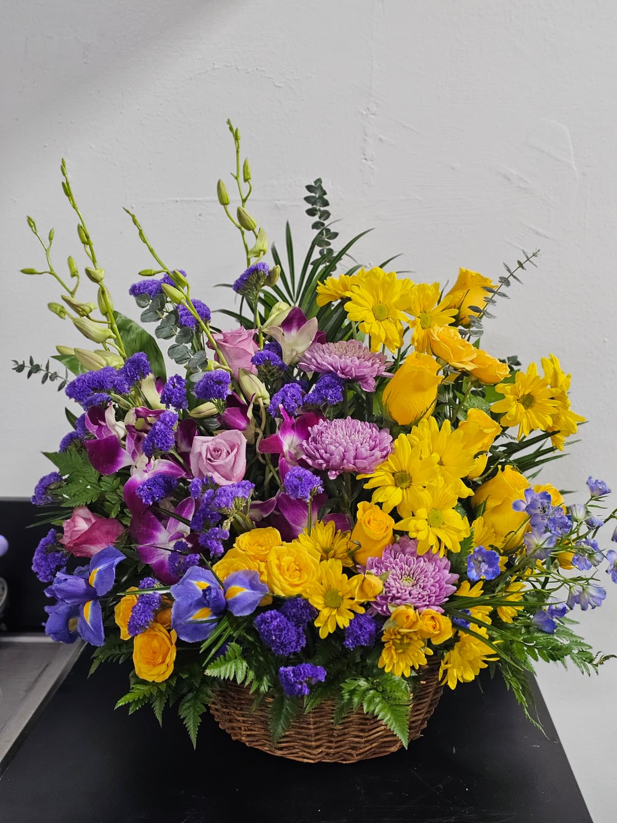 Basket arrangement of yellow daisies, purple orchids, and pink roses