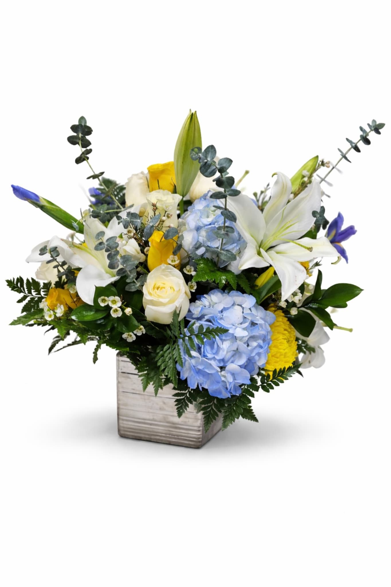 Mixed bouquet with white lilies, blue hydrangeas, and yellow roses in a square vase
