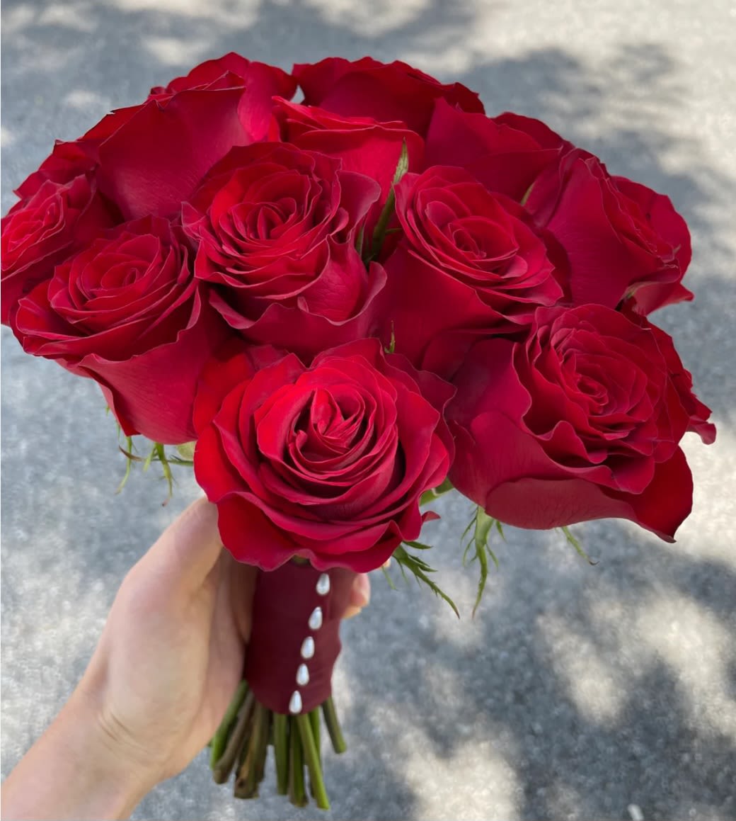 Handheld bouquet of red roses with a burgundy ribbon wrap