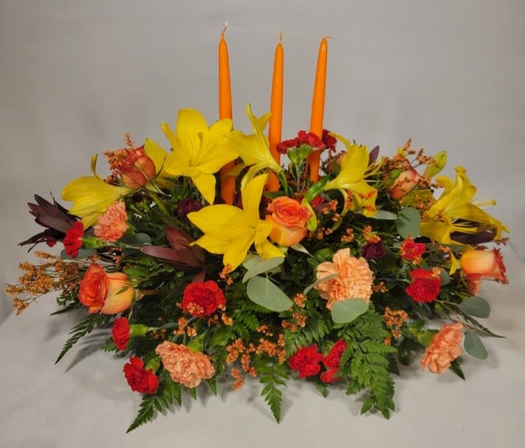 Low floral centerpiece with yellow lilies, orange roses, and orange candles