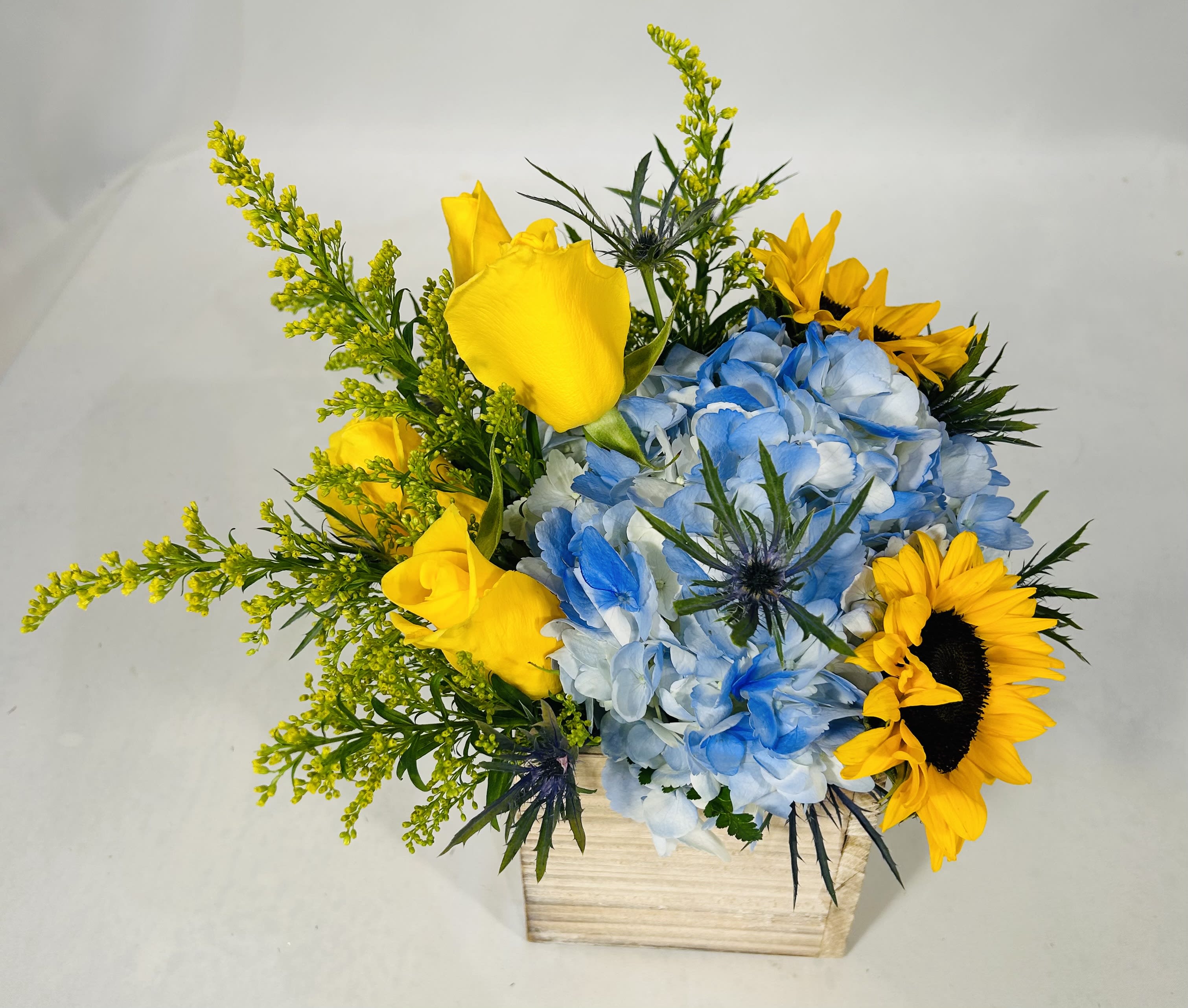 Yellow roses and sunflowers with blue hydrangeas in a wooden box