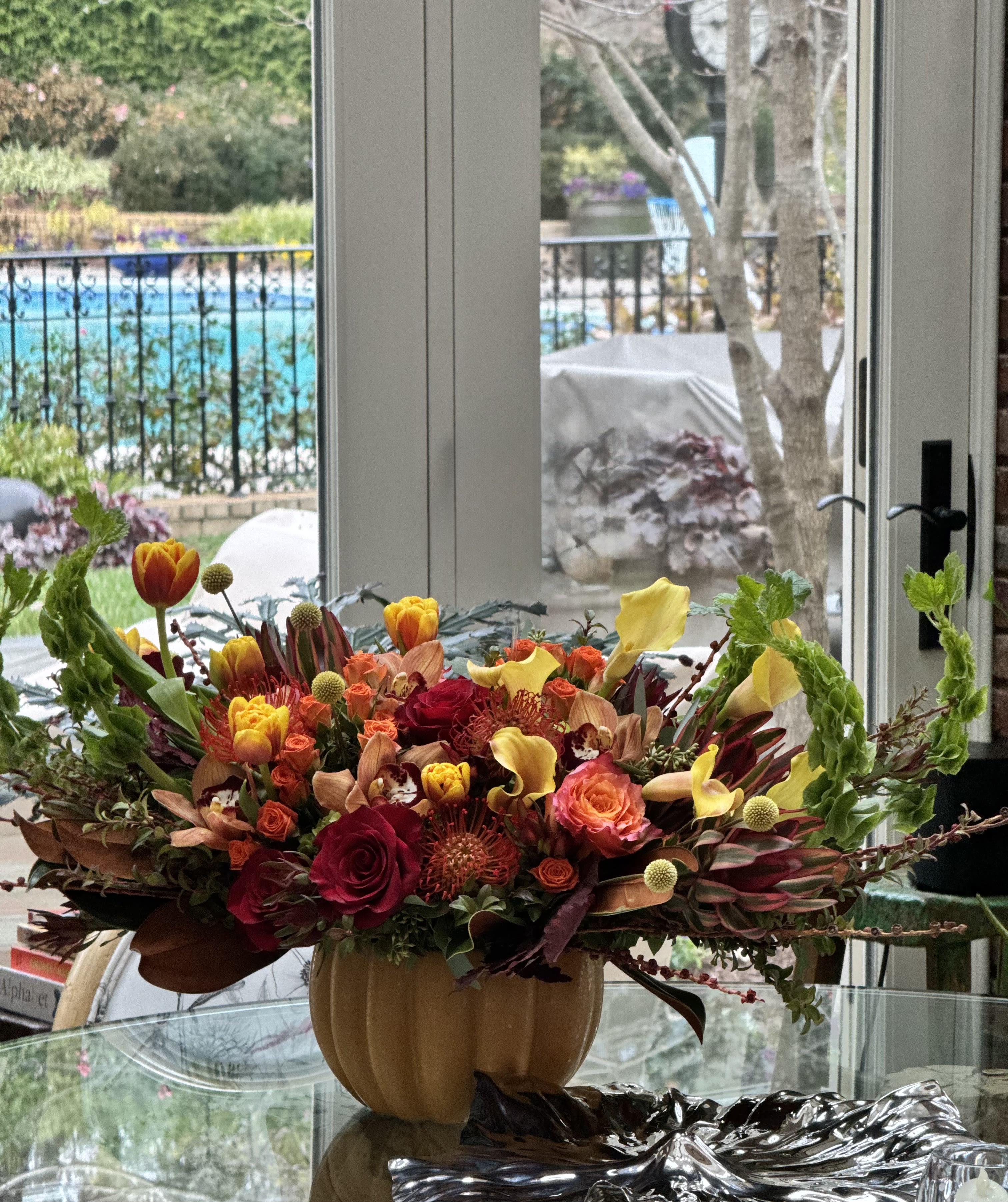 Autumn floral arrangement in a pumpkin-shaped vase with red, orange, and yellow blooms