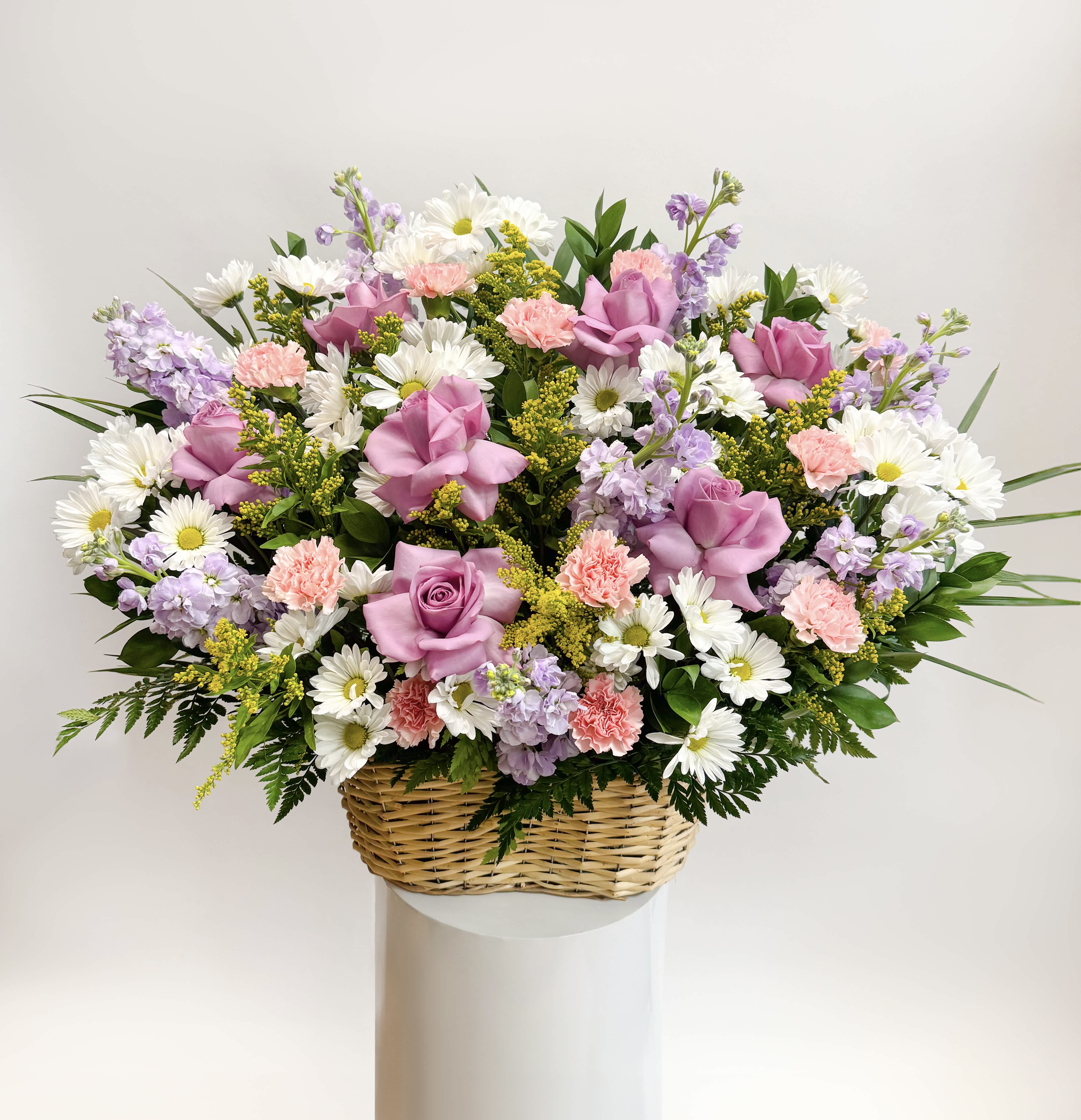 Basket arrangement of pink roses, daisies, carnations, and lavender flowers