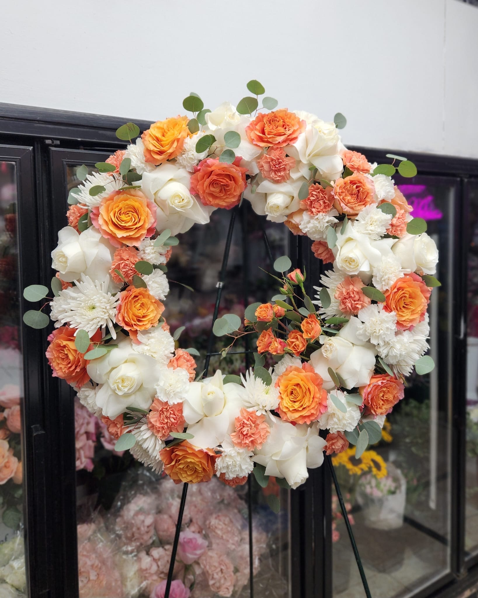 Round floral wreath of orange, white, and peach blooms on a stand