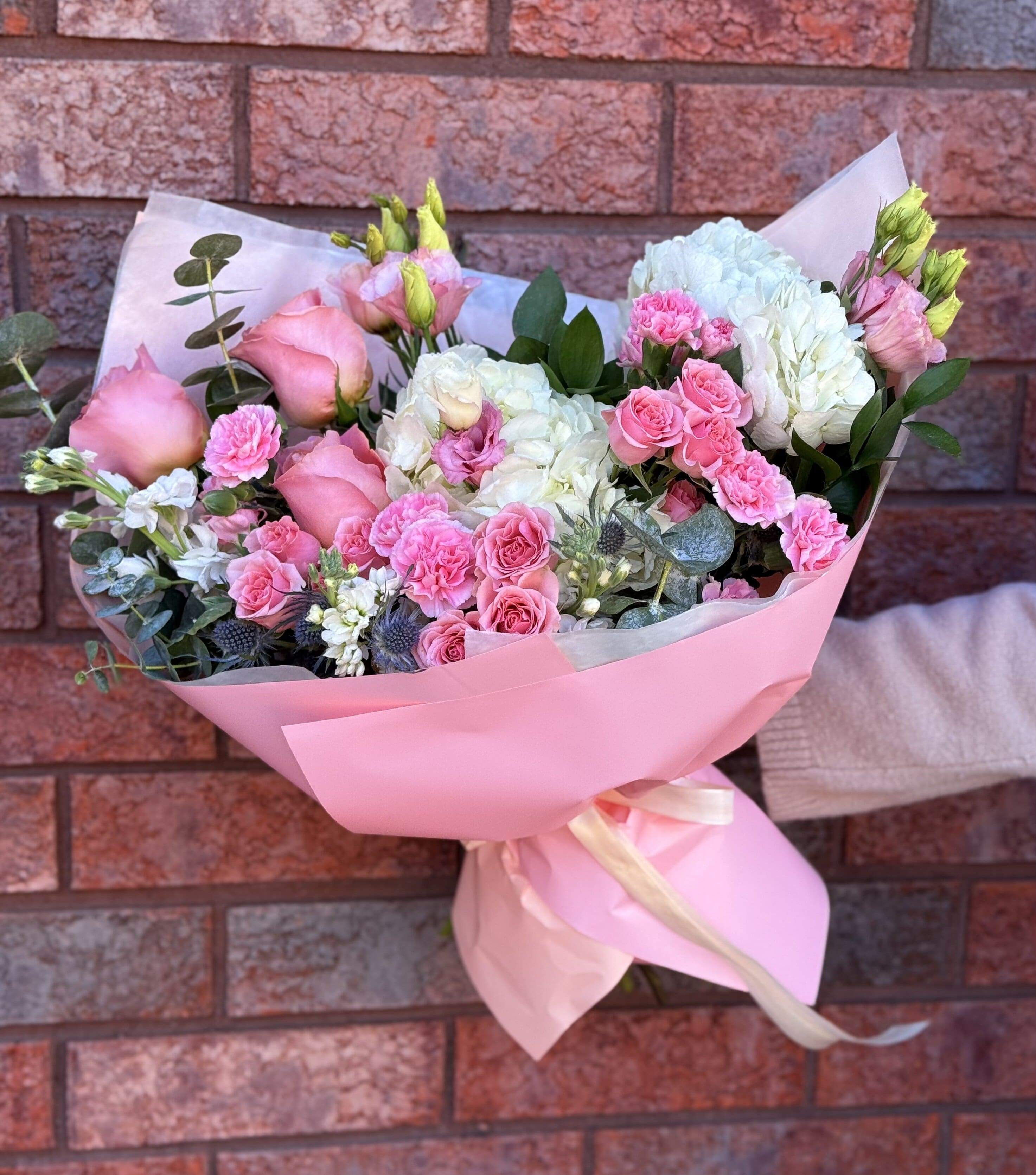Pink and white bouquet of roses, carnations, and hydrangeas wrapped in pink paper