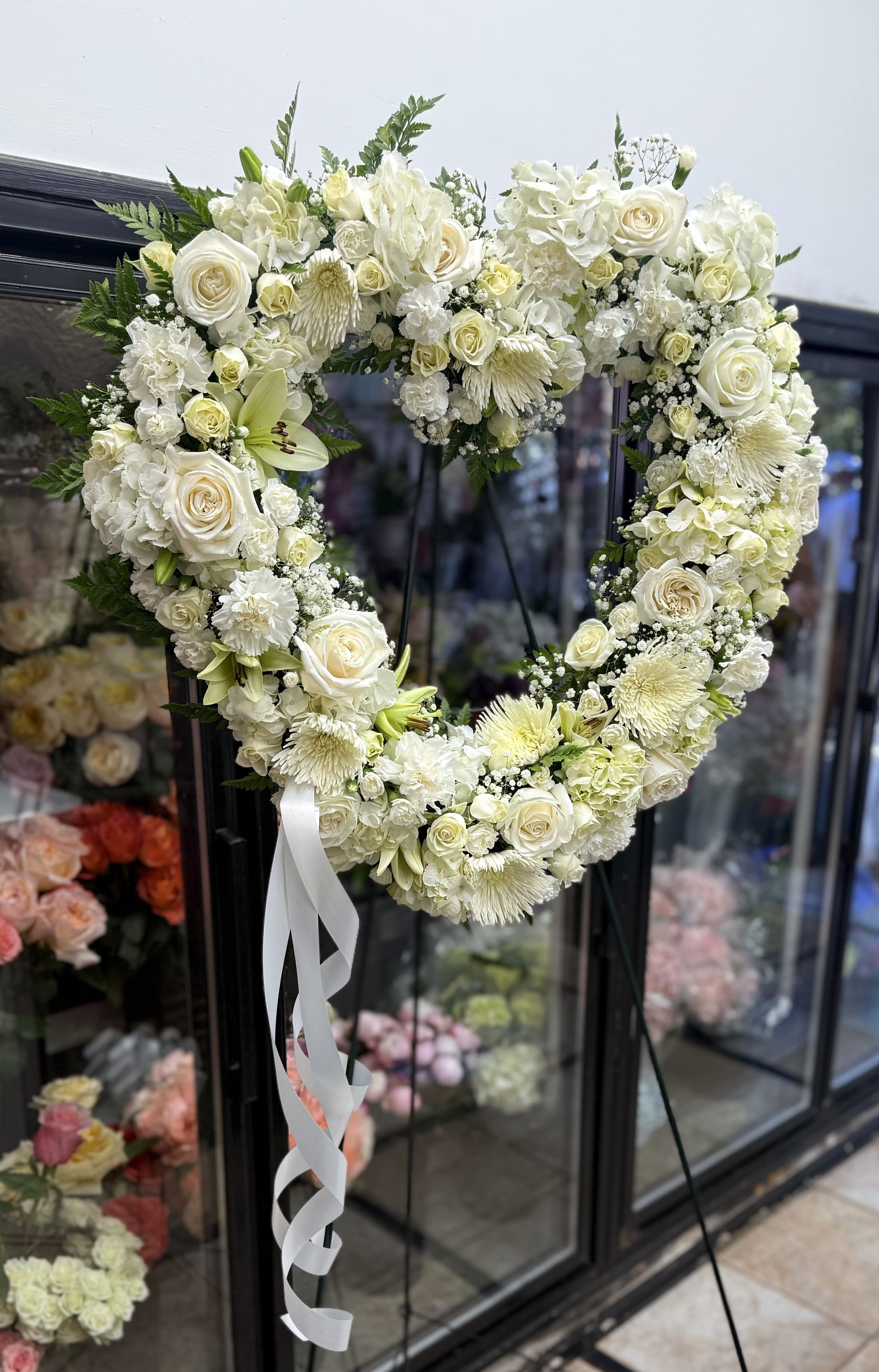 Heart-shaped white floral wreath with a white ribbon bow