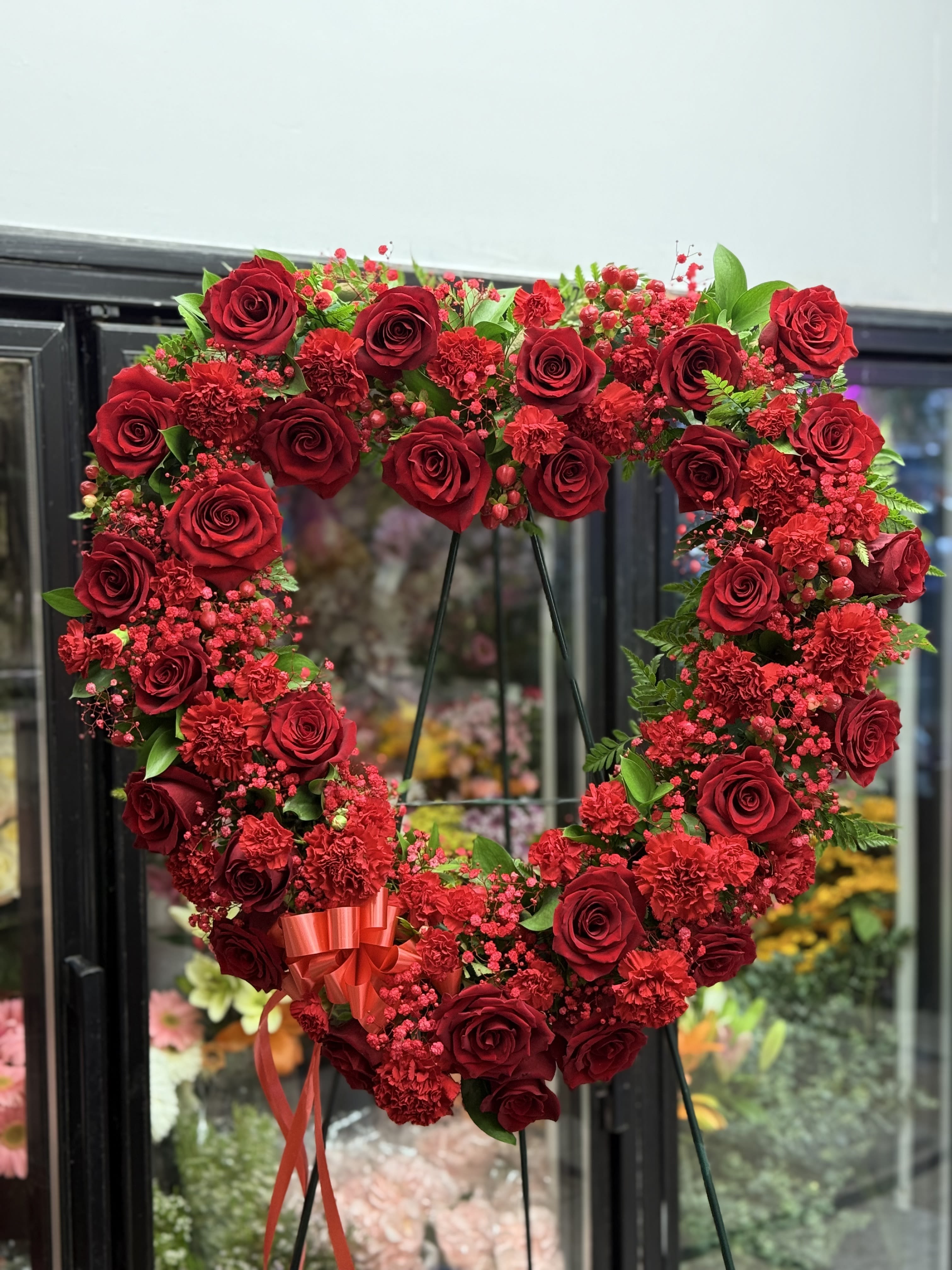 Heart-shaped red rose wreath on a stand with a ribbon bow
