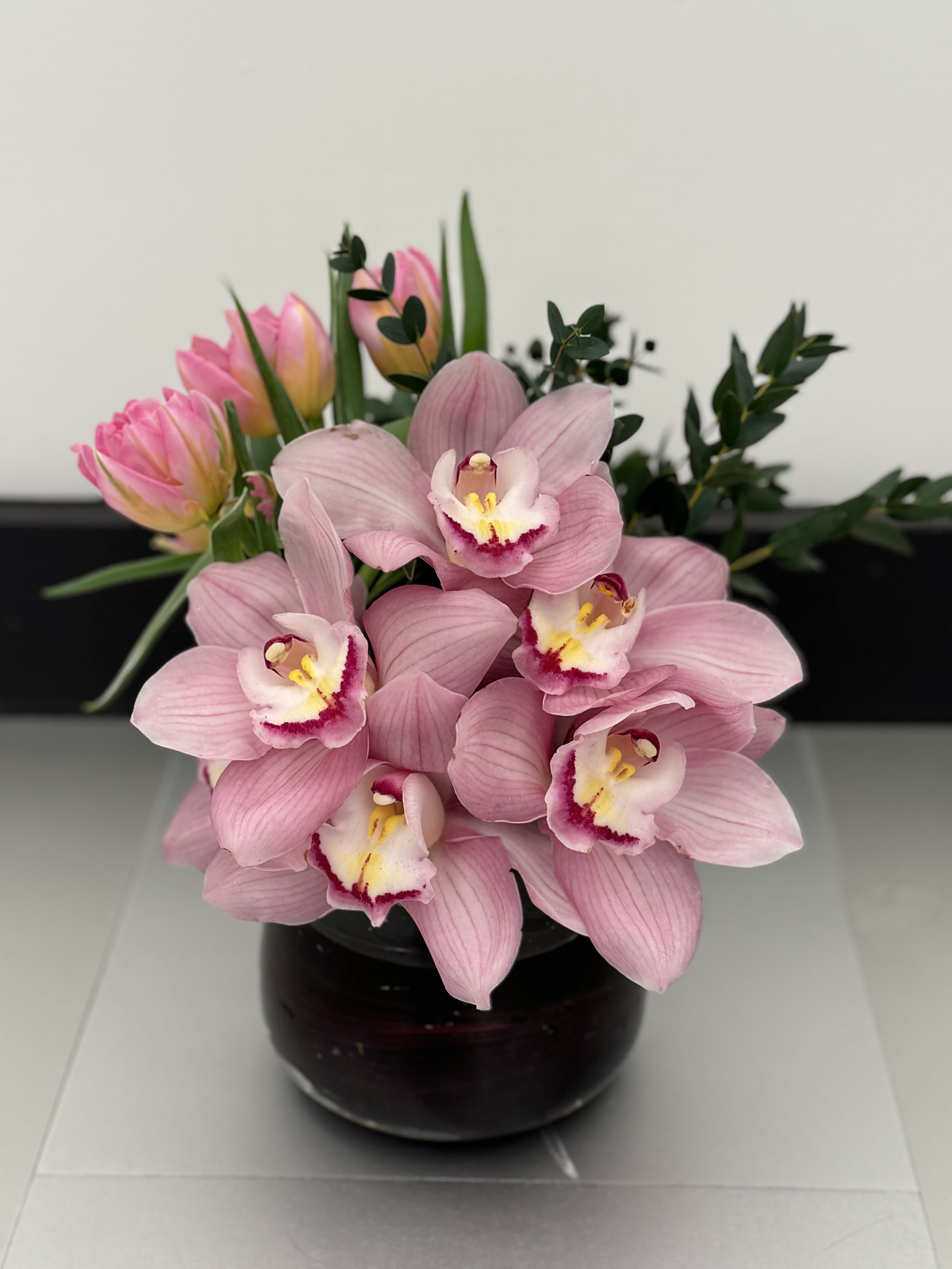 Pink orchids and tulips arranged in a dark glass vase