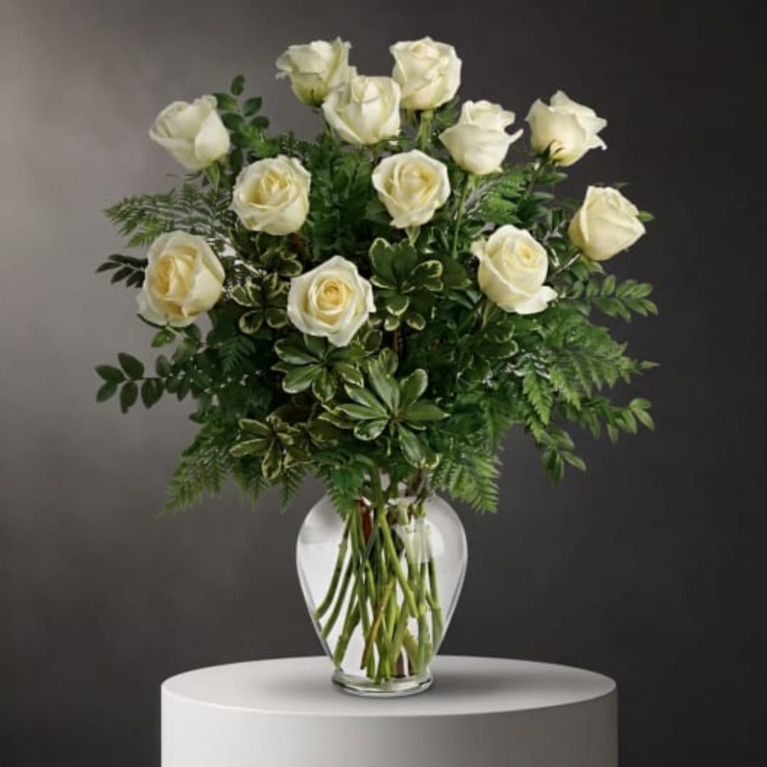 White roses arranged in a clear glass vase with mixed greenery