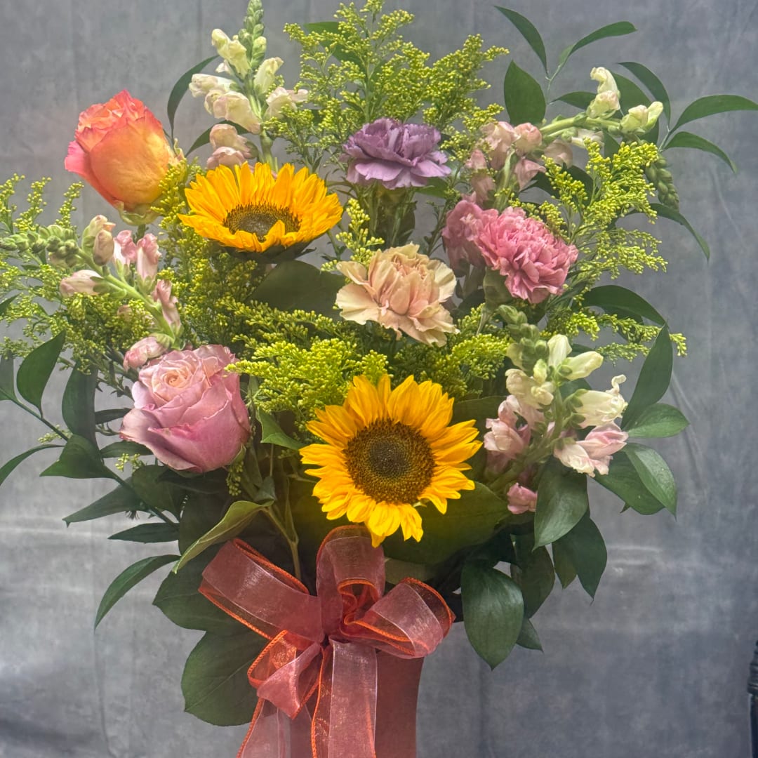 Mixed bouquet with sunflowers, roses, and carnations tied with a pink ribbon