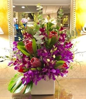 Tall mixed bouquet of purple and red flowers in a white vase