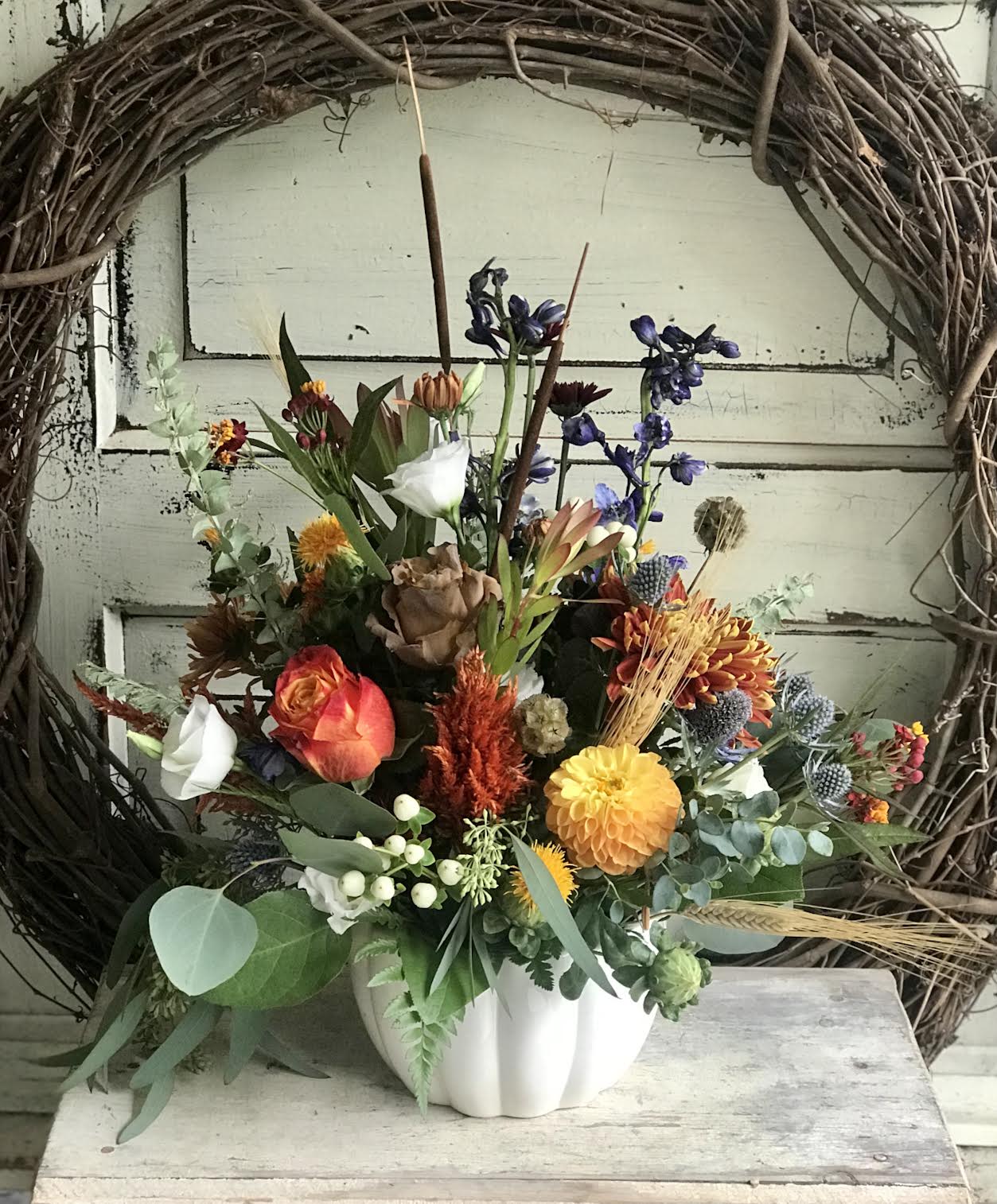 Mixed floral arrangement in a white pumpkin-shaped vase with orange, yellow, and purple blooms