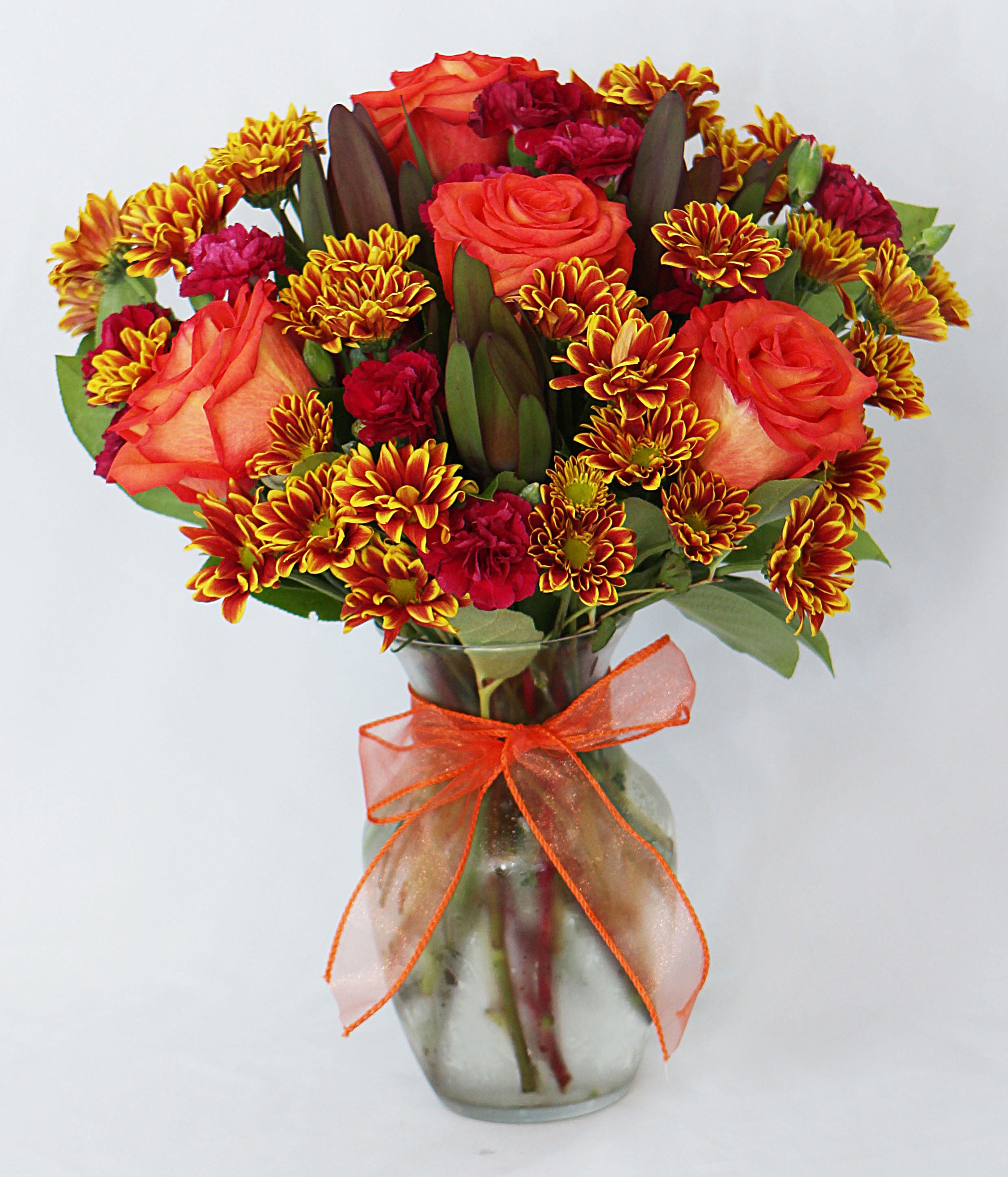 Bouquet of orange roses and red chrysanthemums in a glass vase with an orange ribbon