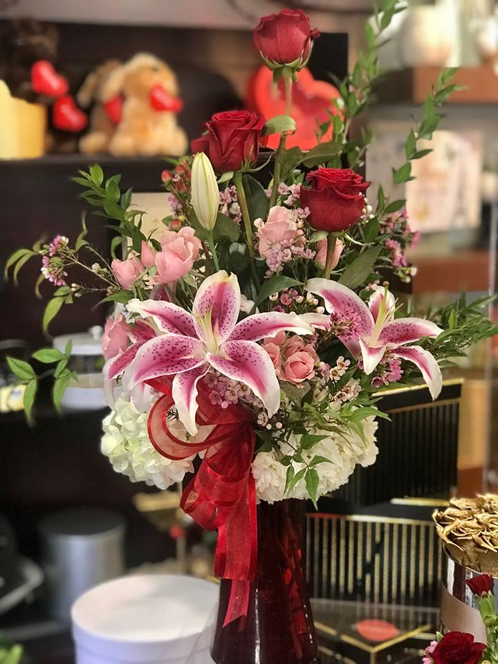 Bouquet of red roses and pink lilies in a tall vase with a red ribbon