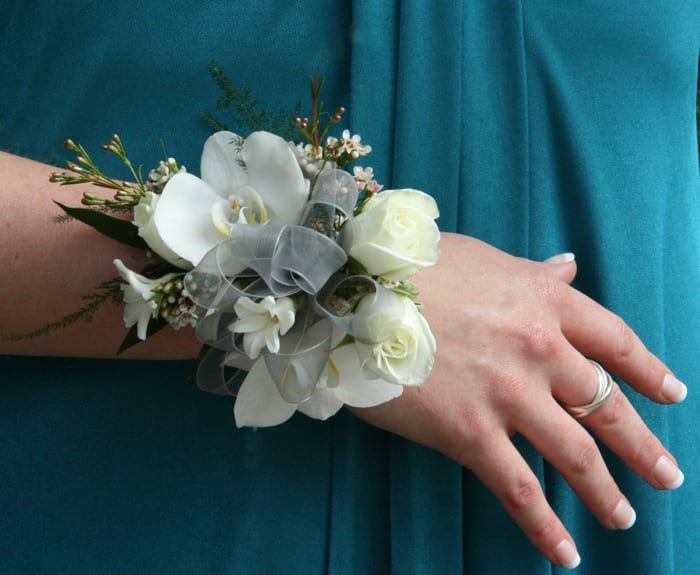 White floral wrist corsage with ribbon on a person's wrist