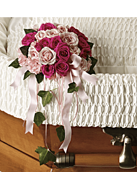 Pink and white rose bouquet with ribbon draped over a white casket