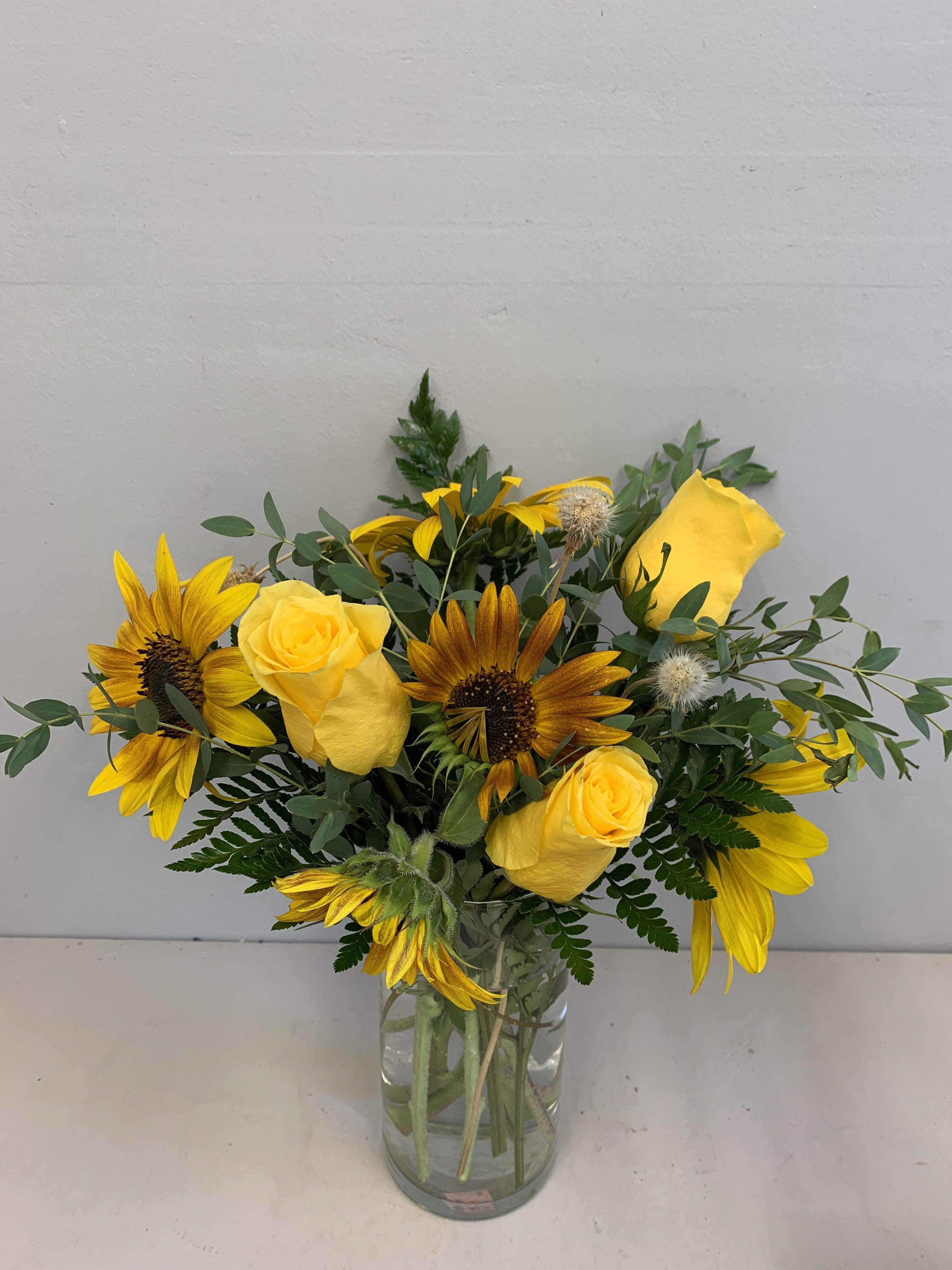 Sunflowers and Roses - Such delightful flowers arranged in a rectangle glass vase, bright yellow sunflowers surrounded by green bluperium, cream roses, yellow button poms and mini green carnations. A soft hued sweet arrangement created just for that special occasion.