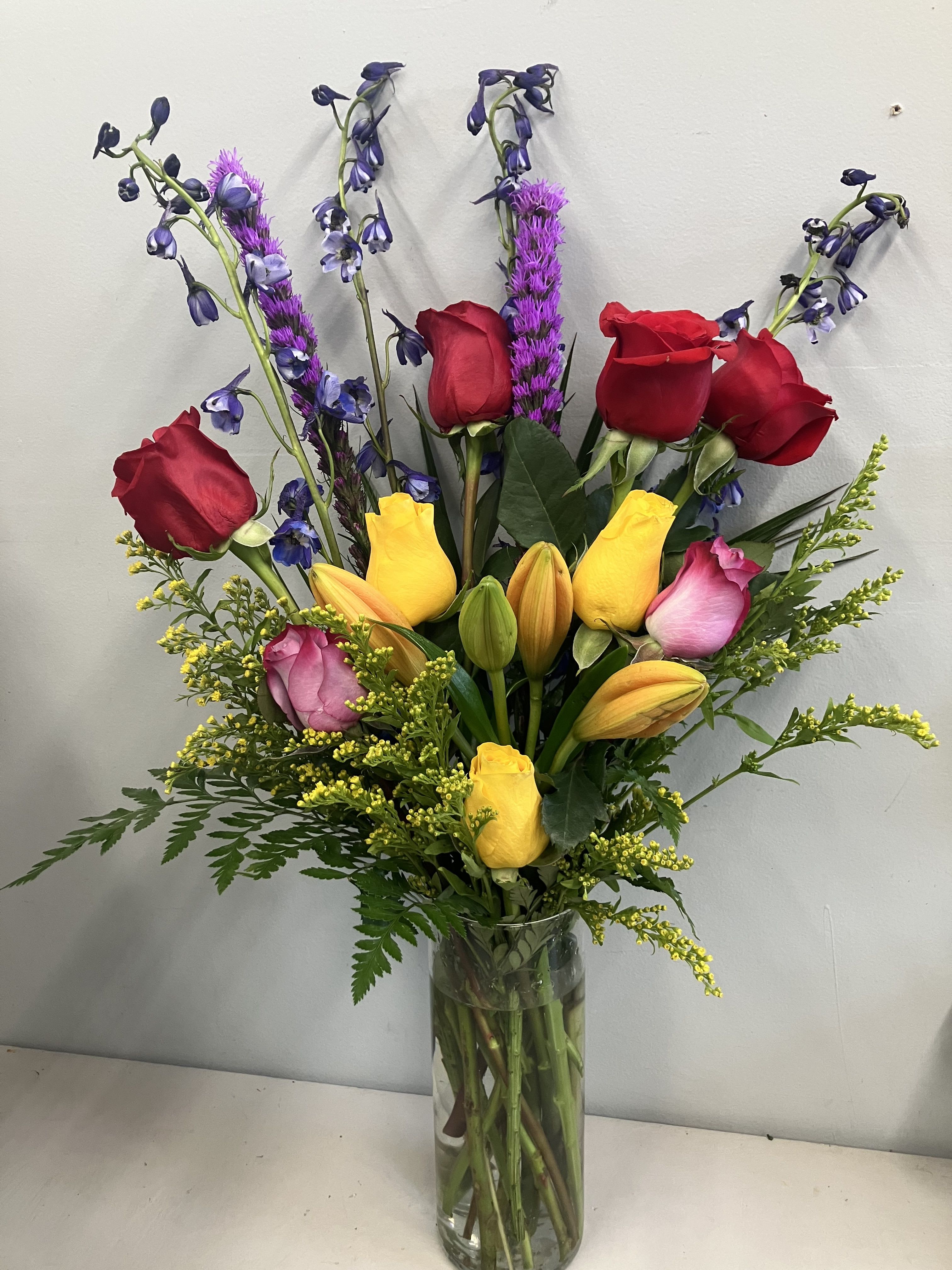 Tall bouquet of red and yellow roses with purple accents in a clear glass vase