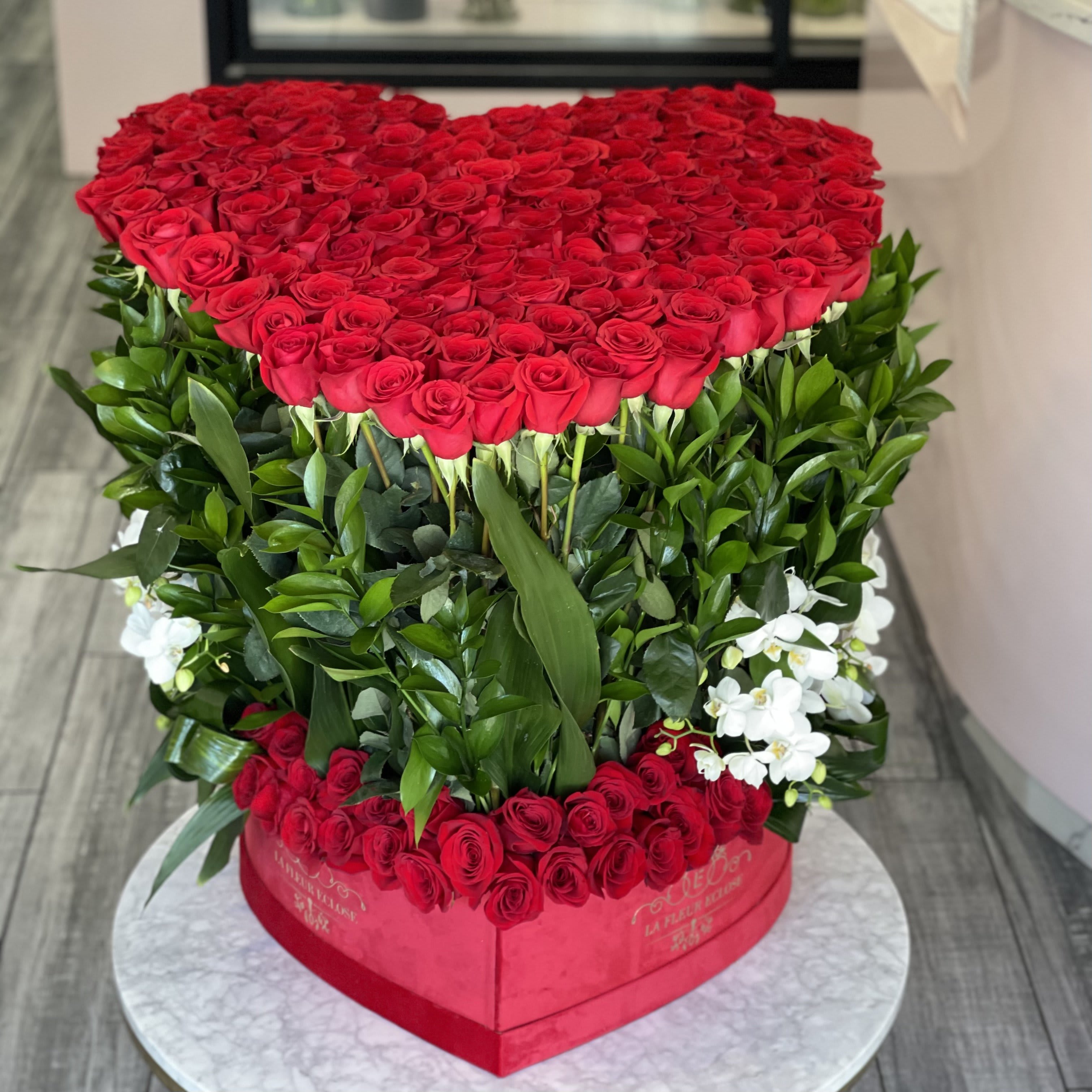 Heart-shaped arrangement of red roses with white orchids in a red box