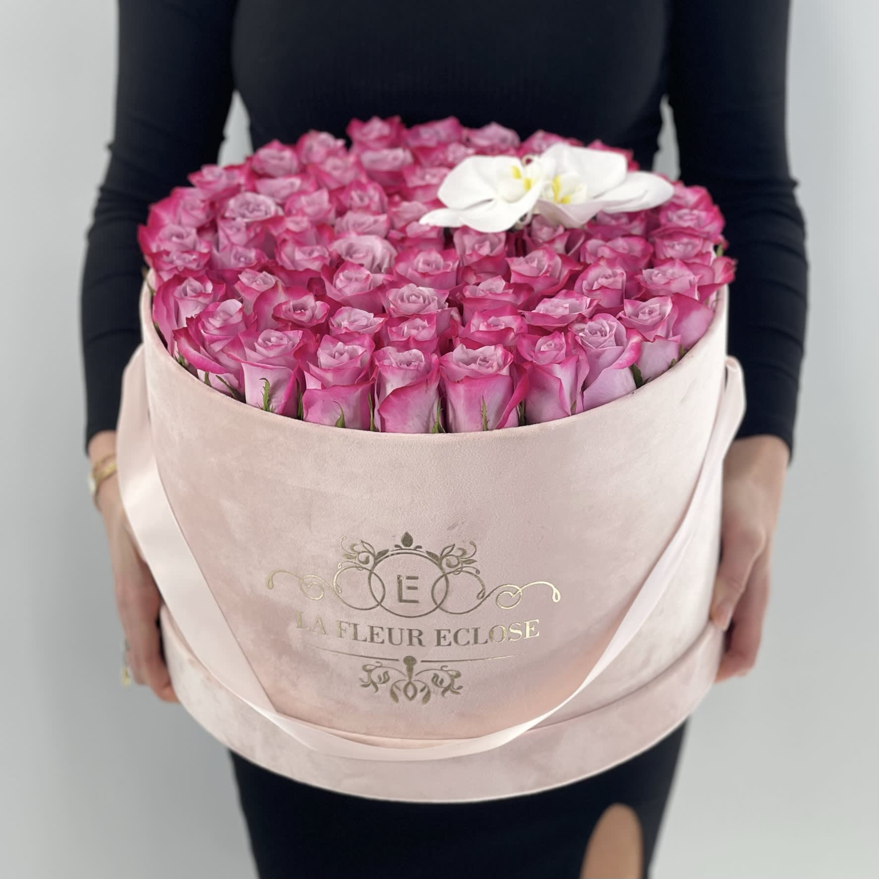 Round box of pink roses with a white orchid accent