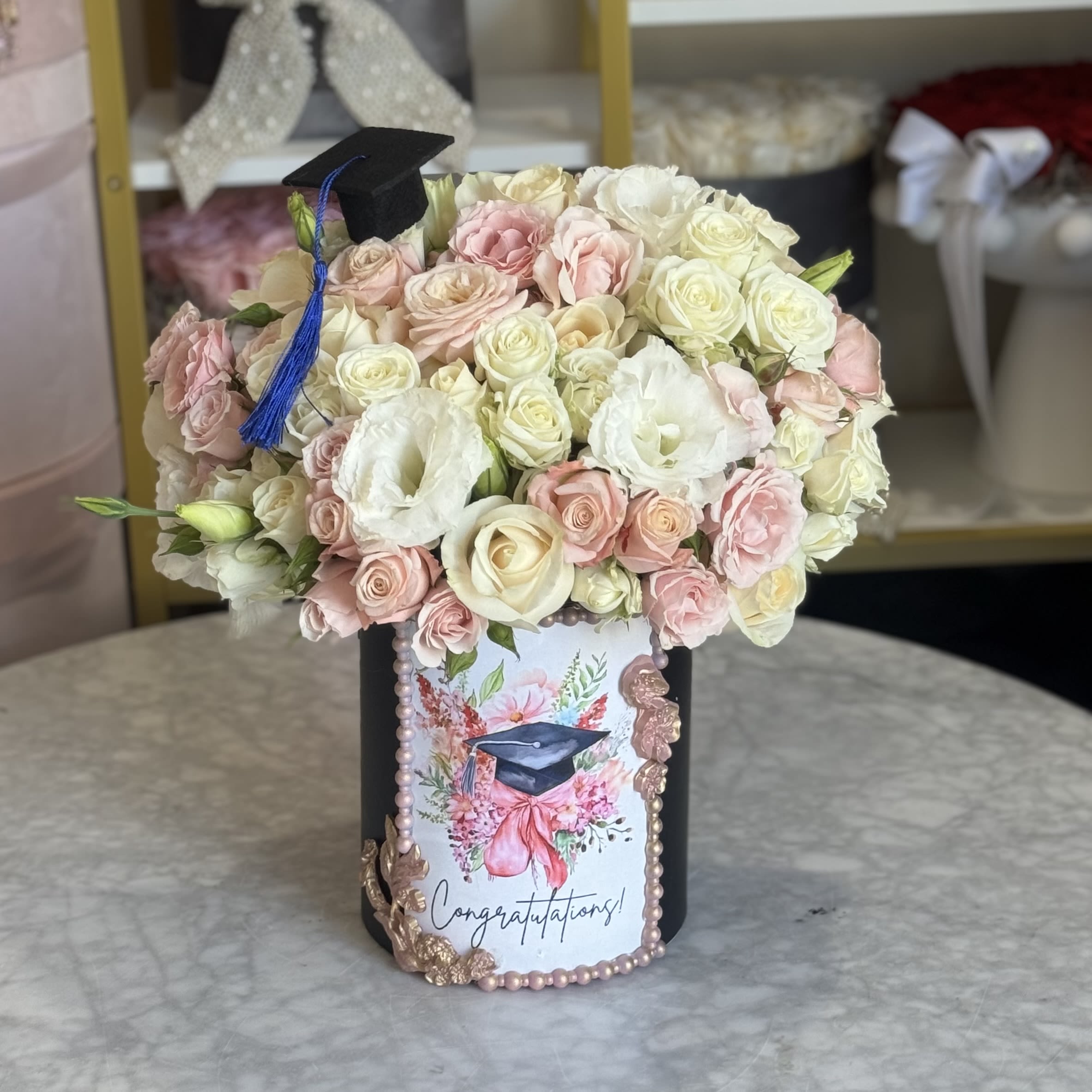 Blossoming Graduation Box - Celebrate a milestone with elegance and beauty! Our Blossoming Graduation Box is a stunning arrangement of premium roses in soft blush, ivory, and cream tones—expertly handcrafted to honor your graduate’s big day.  Presented in a luxurious hatbox adorned with a miniature graduation cap and a custom “Congratulations!” design, this floral gift is perfect for expressing pride, joy, and best wishes. Ideal for high school, college, or university graduations.  Make their achievement bloom forever  