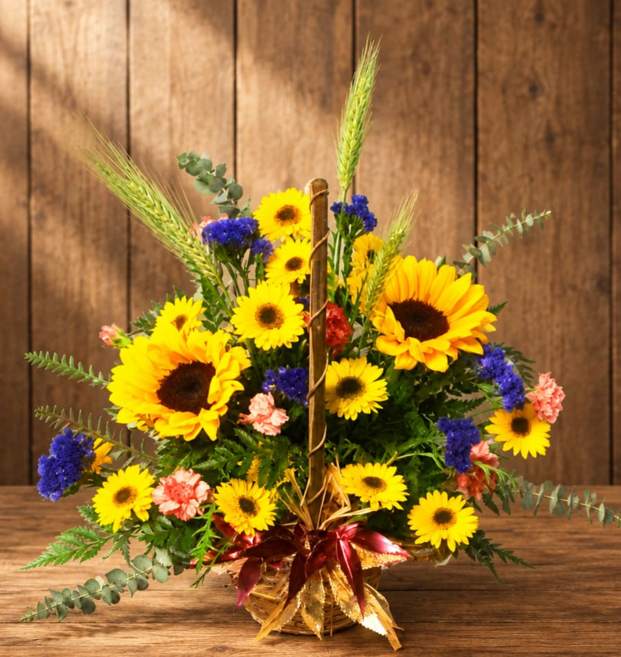 Basket arrangement of yellow sunflowers, blue flowers, and pink carnations
