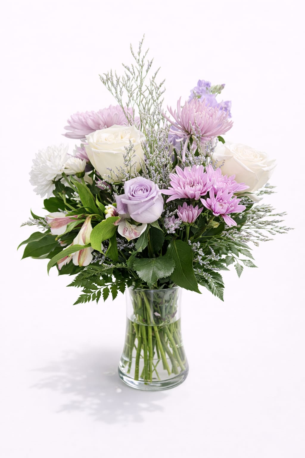 Lavender Grace Gathering Bouquet - Roses, Chrysanthemums &amp; Stock - Soft lavender and creamy white blooms gather into a tender arrangement that feels like a quiet embrace-the Lavender Grace Gathering Bouquet is a flower arrangement perfect for a birthday, a get well wish, or a heartfelt thank you. Featuring roses and chrysanthemums alongside airy stock, this bouquet reads as both celebratory and consoling, making it equally suited for sympathy and funeral tributes or a gentle anniversary surprise for the person you're thinking of.  Creamy white roses pair with soft lavender roses and fluffy lavender chrysanthemums, while delicate stock and alstroemeria add slender, fragrant accents and subtle pink-tinted highlights. The flowers are arranged in a flared clear glass vase that shows off the stems and keeps the design feeling open and relaxed; fine, mist-like filler adds texture without overwhelming the main blooms. Dimensions are balanced for bedside or tabletop display-the rounded shape creates a calm, tender presence that fills a room without shouting.  Send this arrangement to make her feel truly seen-whether you're celebrating a quinceañera, marking Mother's Day in Newington, CT, or offering comfort after a loss. Care is simple: keep fresh water in the vase, trim stems every few days, and keep away from direct heat to extend the life of the soft pastel roses, chrysanthemums, stock, and alstroemeria so the sentiment lingers.