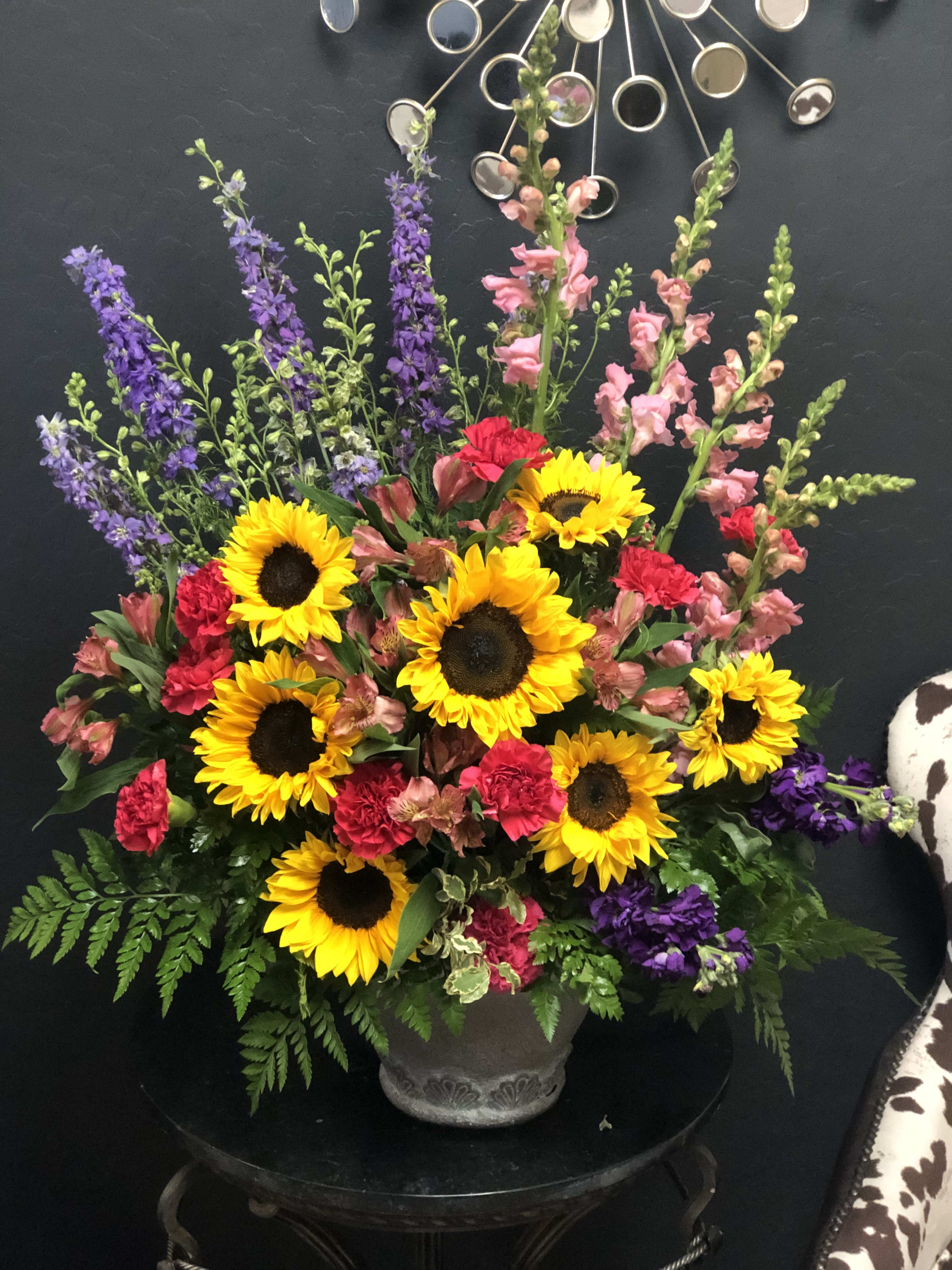 Mixed bouquet with sunflowers, pink carnations, and purple spikes in a gray vase