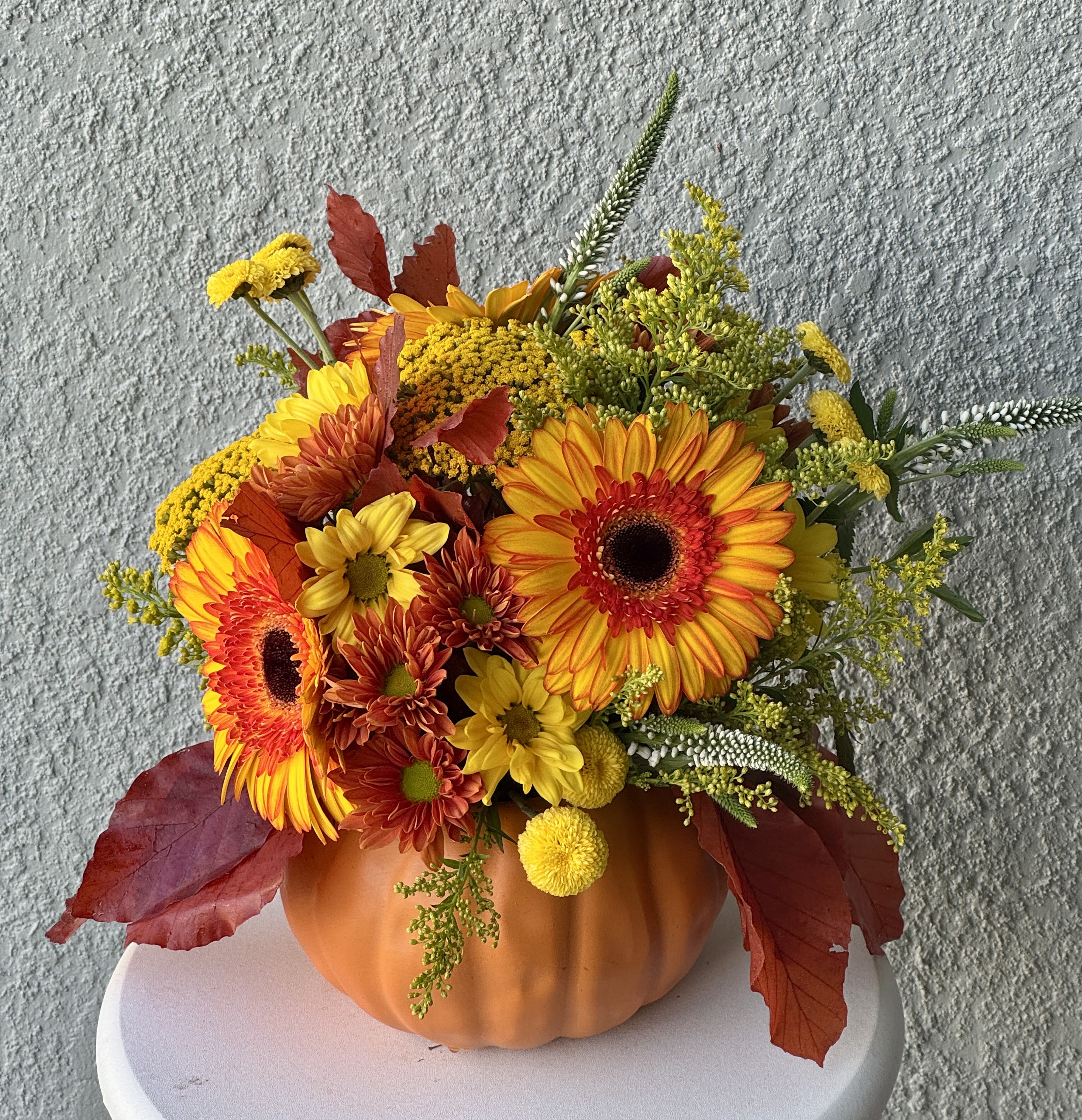 Autumn floral arrangement in a pumpkin-shaped container with orange and yellow blooms