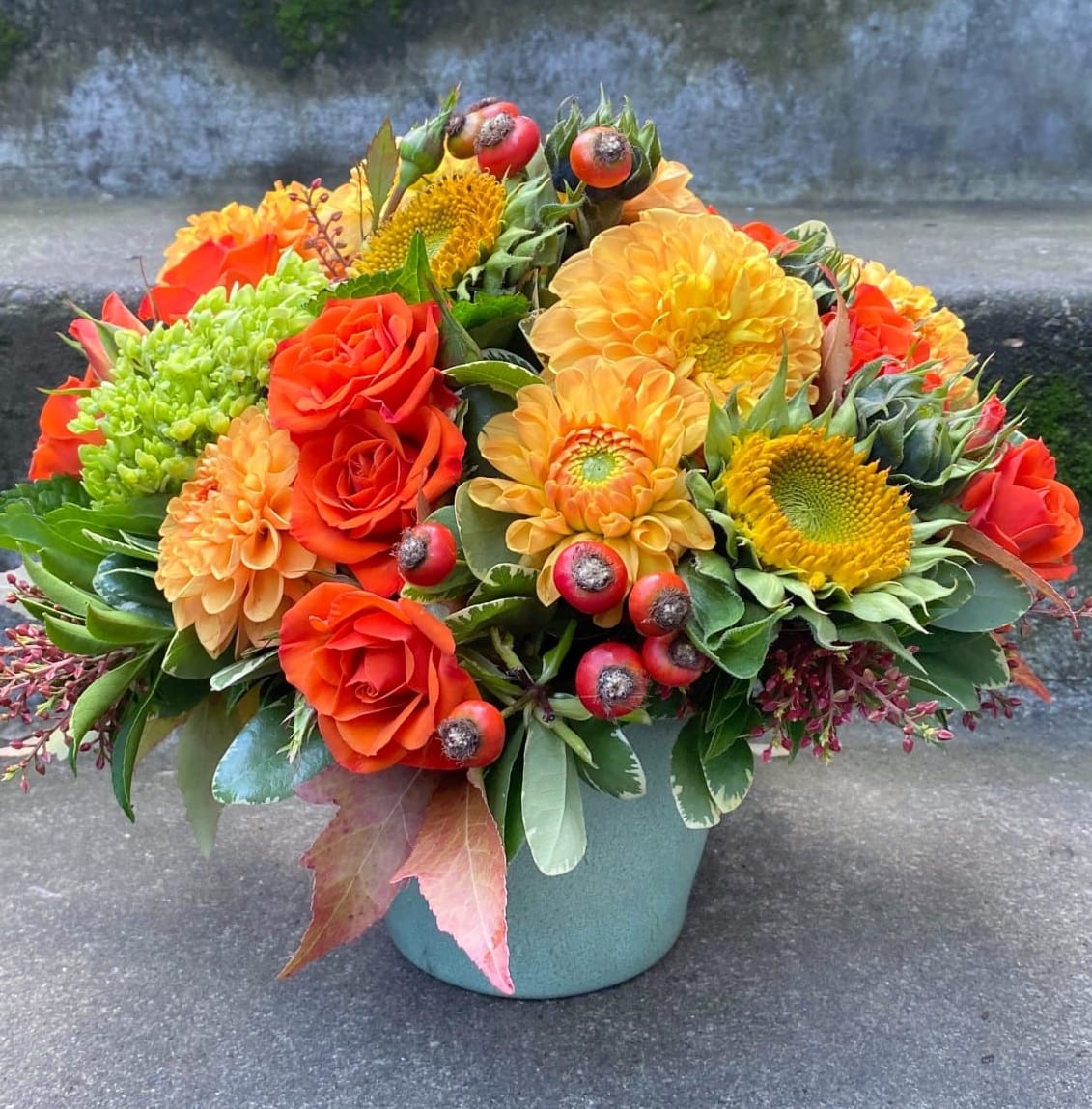 Orange and yellow flower arrangement in a teal container