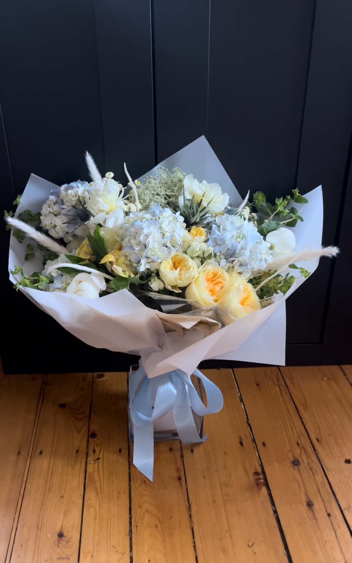 Bouquet of white and pale yellow flowers wrapped in white paper with a blue ribbon