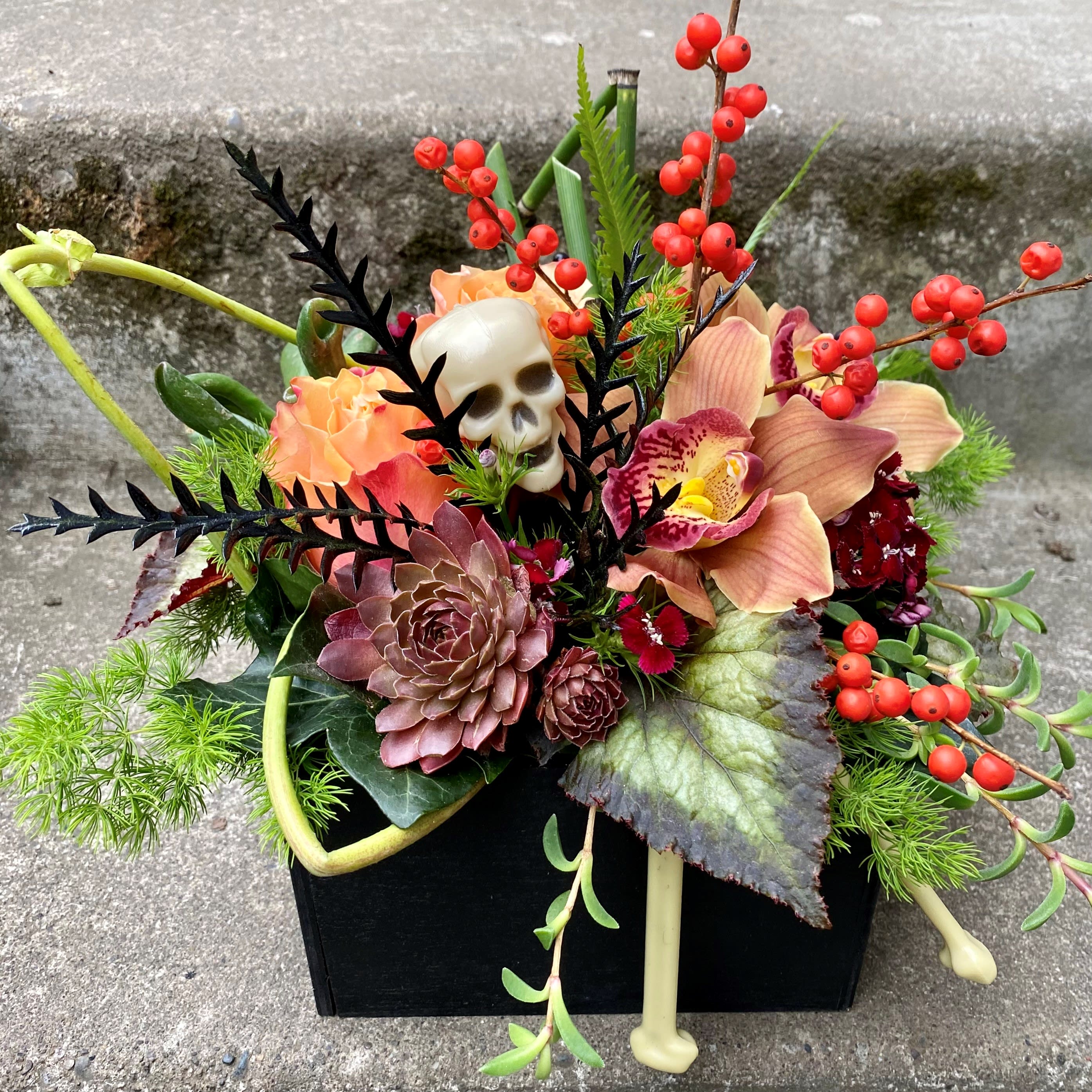 Halloween floral arrangement with a skull and orange orchids in a black container
