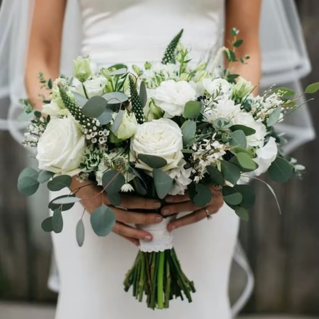 Bride holding a white bouquet with roses and greenery